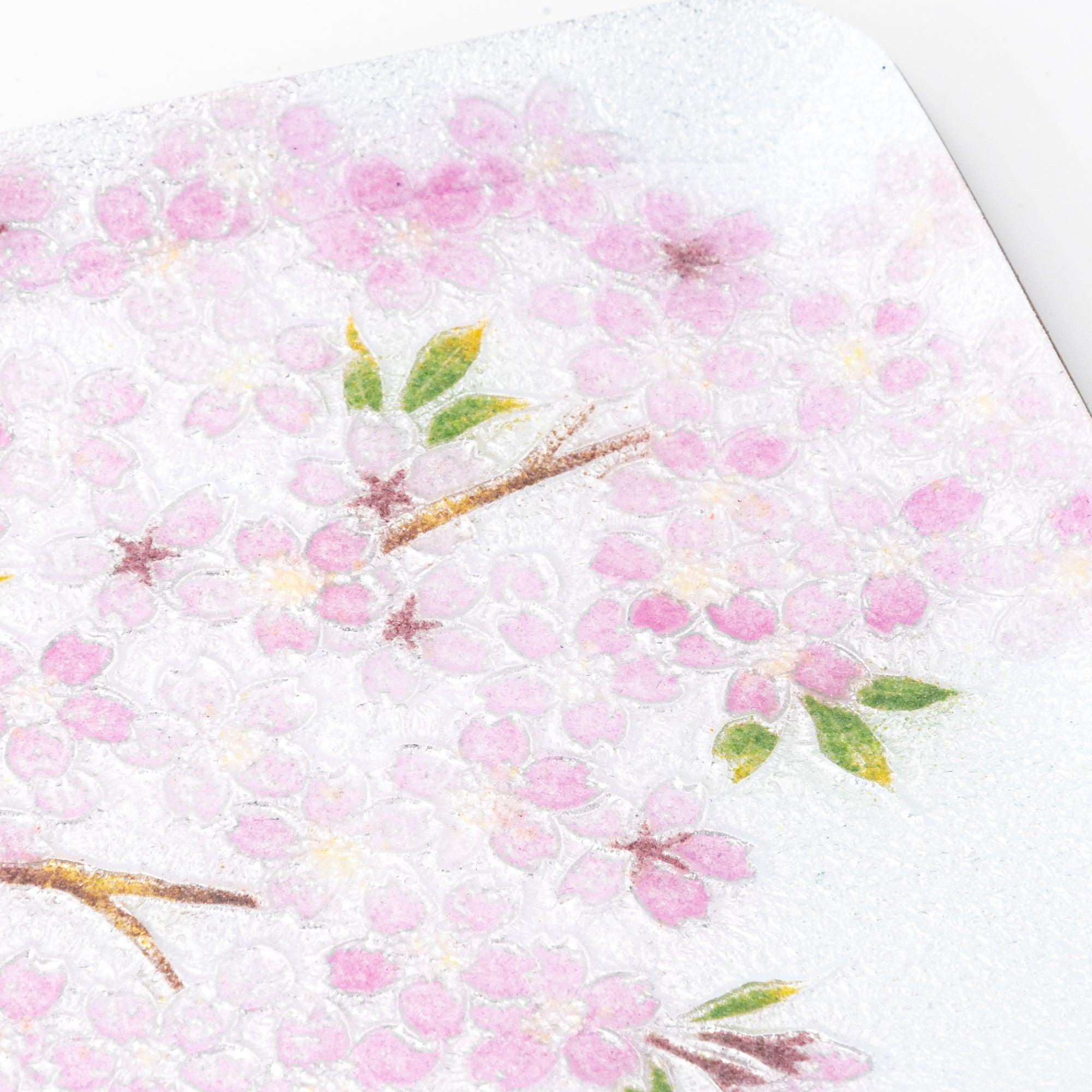 Close-up of the pink cherry blossom design on a textured silver tray, showcasing delicate floral details and green leaves.  