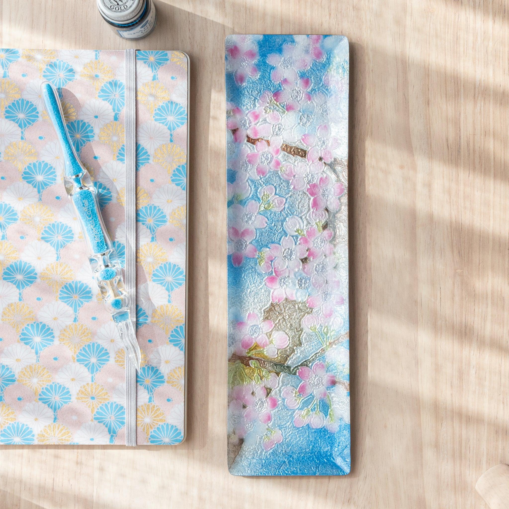 Close-up of tray featuring a delicate pink cherry blossom design on a textured blue background, highlighting fine petal and branch details.