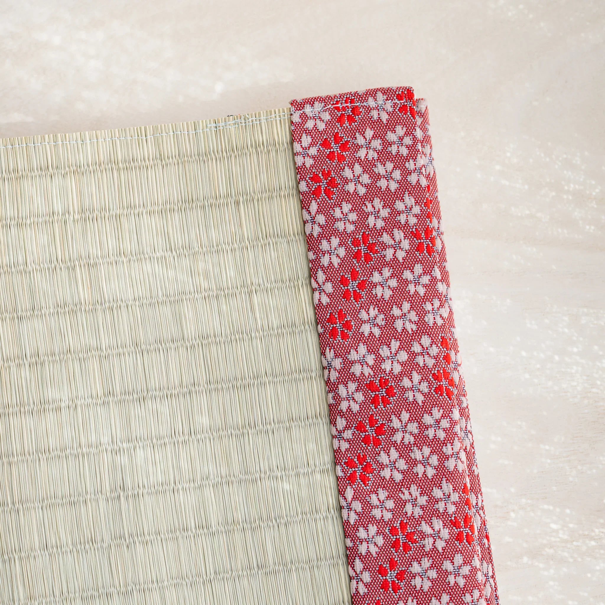 Close-up of pink and red Japanese cherry blossom brocade band beside woven green rush straw at the cover corner
