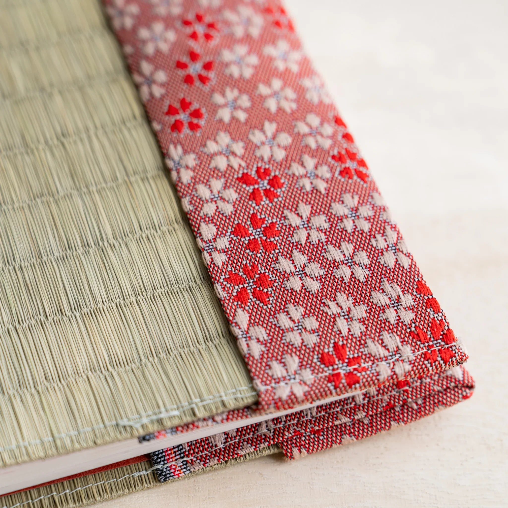 Angled close-up of the cherry blossom brocade band and stitched edge of the tatami book cover over notebook pages