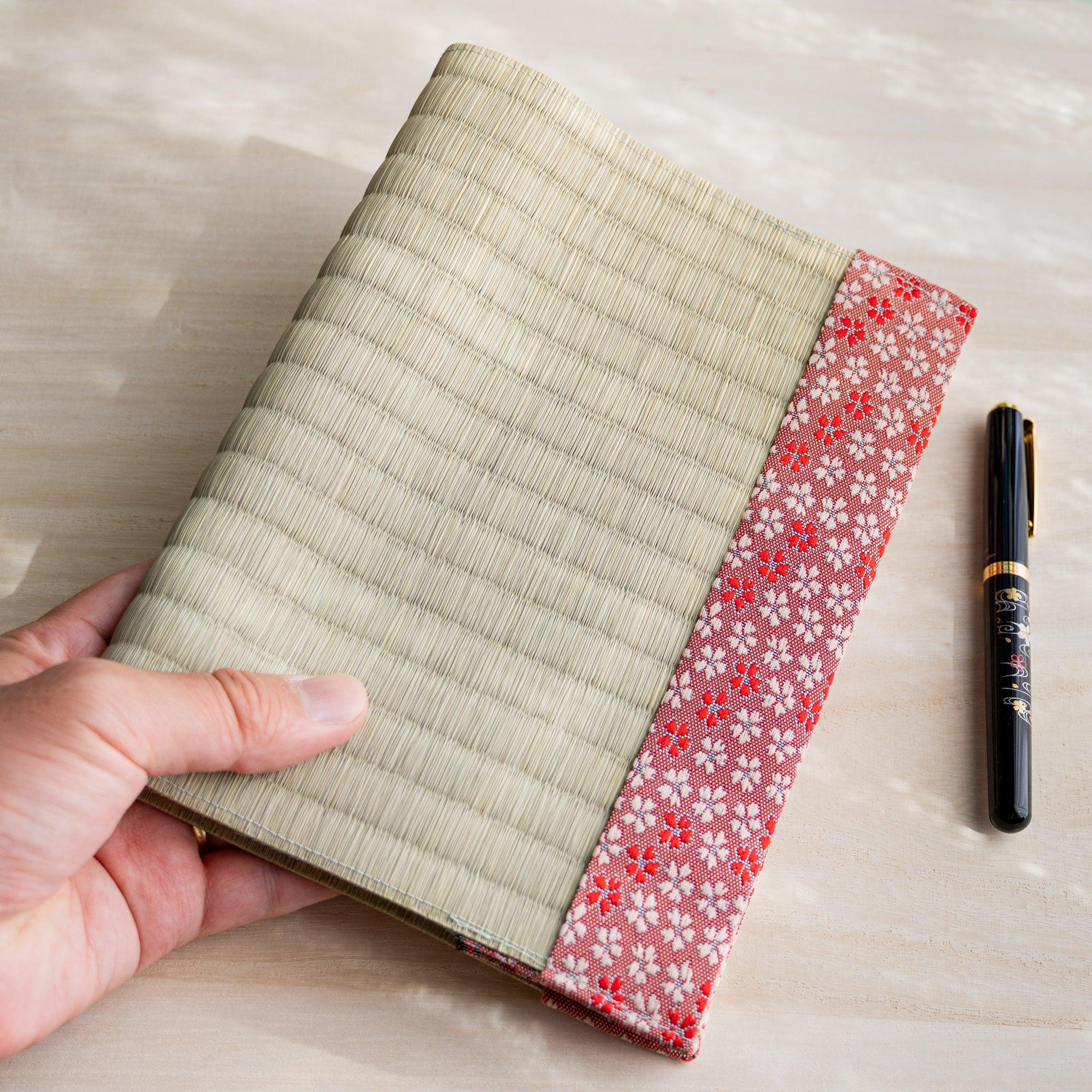 Hand holding closed Sakura tatami book cover with cherry blossom fabric band, black fountain pen on the table