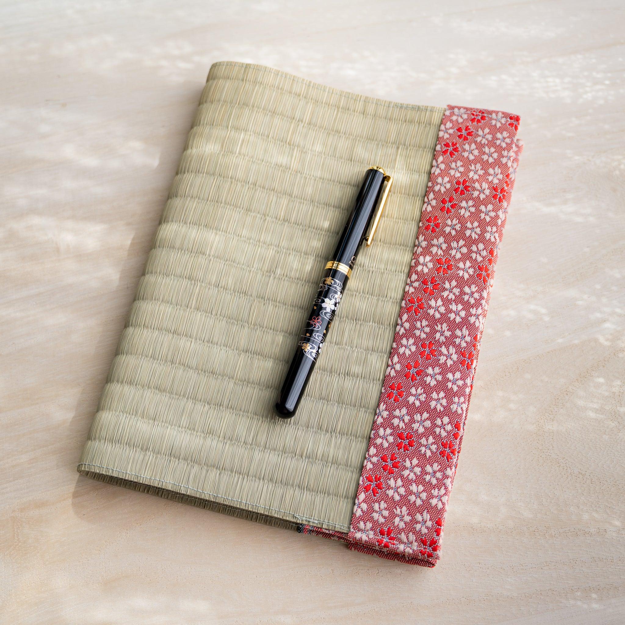 Black and gold fountain pen resting on closed tatami book cover with pink and red cherry blossom fabric band