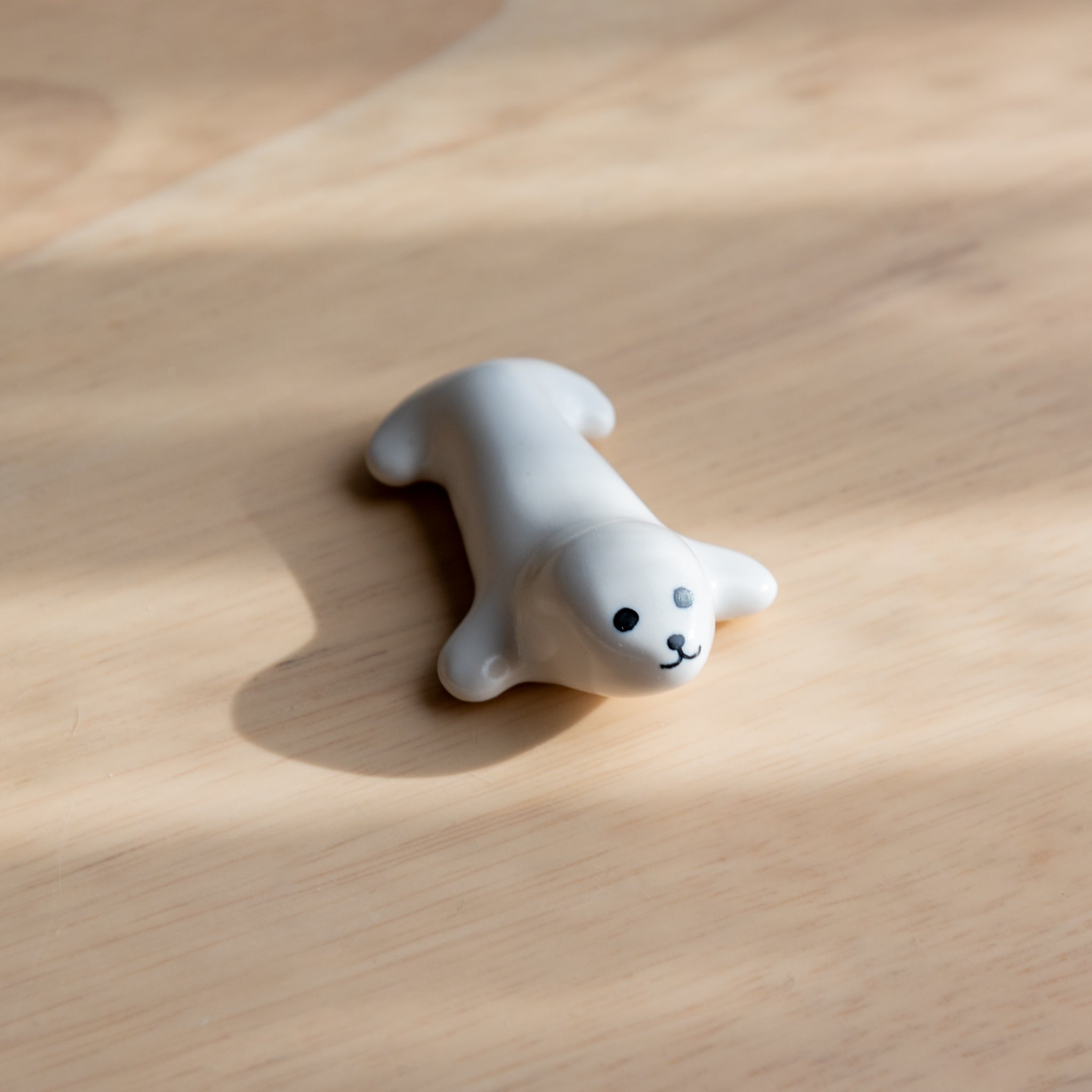 A seal-shaped Japanese ceramic pen rest with a playful design, placed on a wooden surface under soft sunlight.