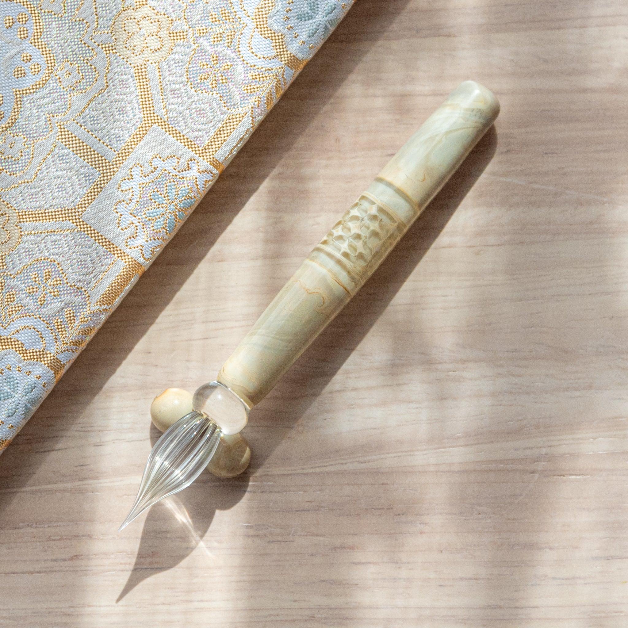 Ivory glass pen with a shippo design, paired with a matching glass pen rest. Displayed on a wooden surface beside a Nishijin textile notebook.