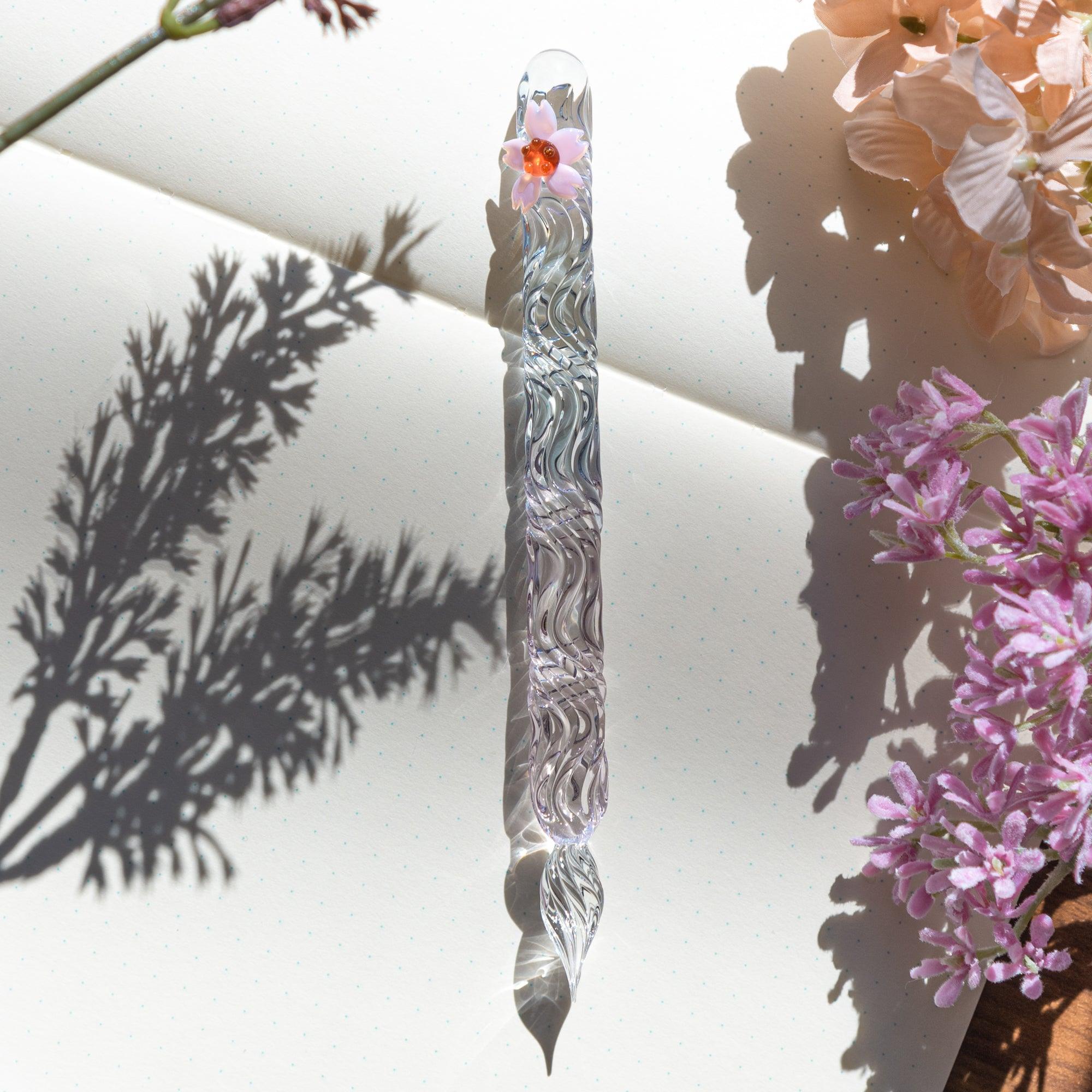 A sakura motif glass pen placed on a notebook, beautifully reflecting light and shadows in an artistic shot.