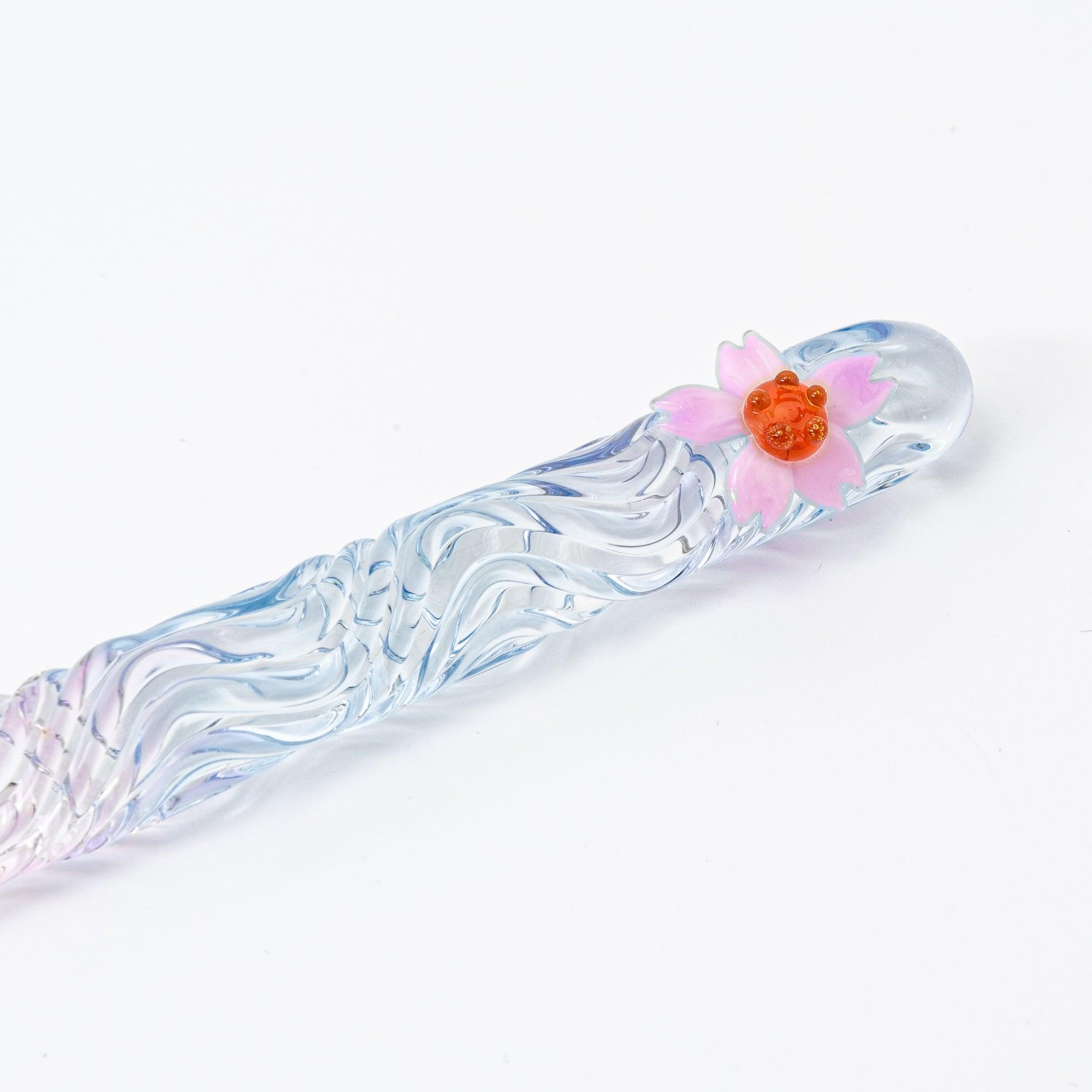 A clear glass pen with a blend of soft pink and blue hues, featuring a delicate sakura flower motif on the handle.