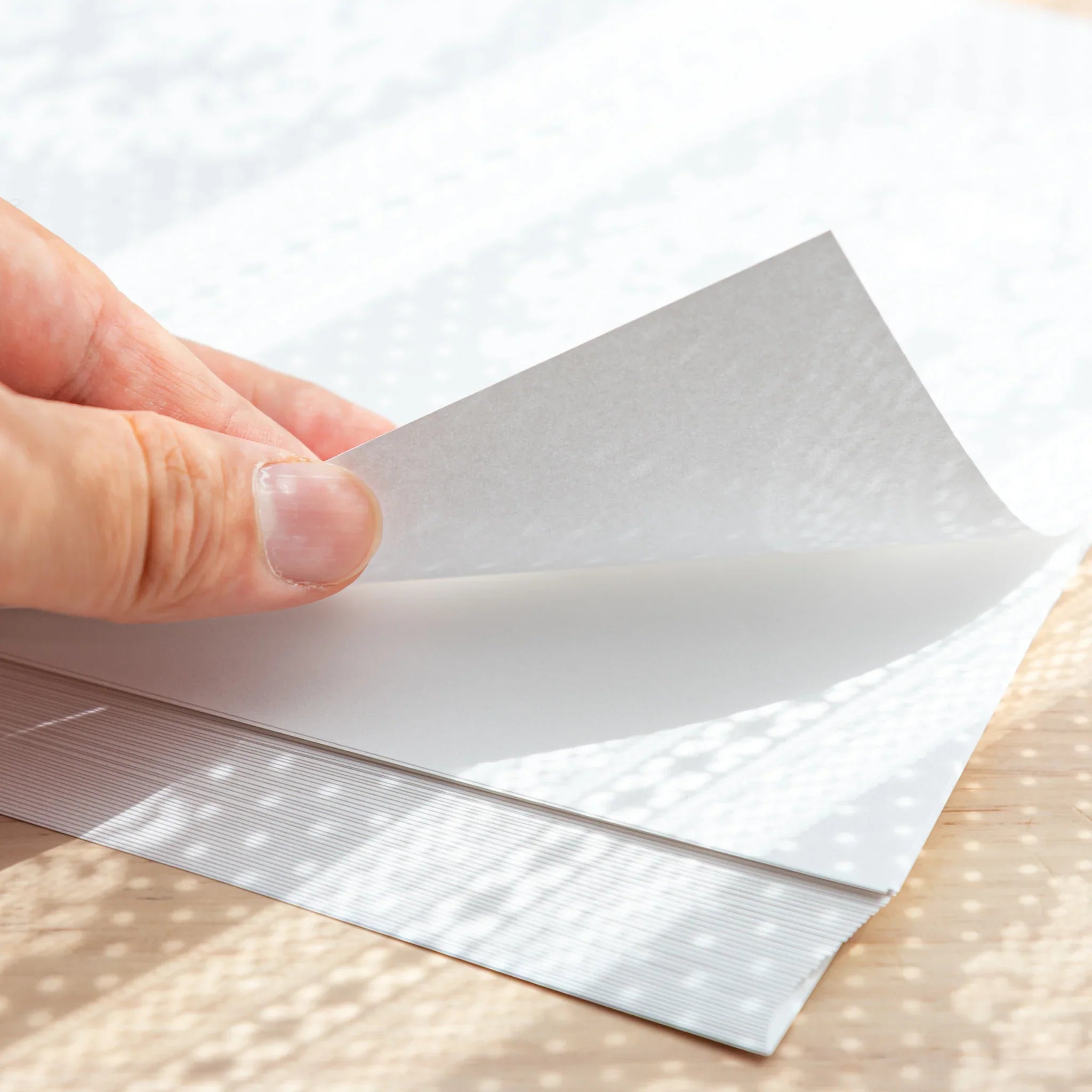 Close-up of slight white Loose Leaf Paper, showing hand lifting thin white sheets with soft texture under sunlight.