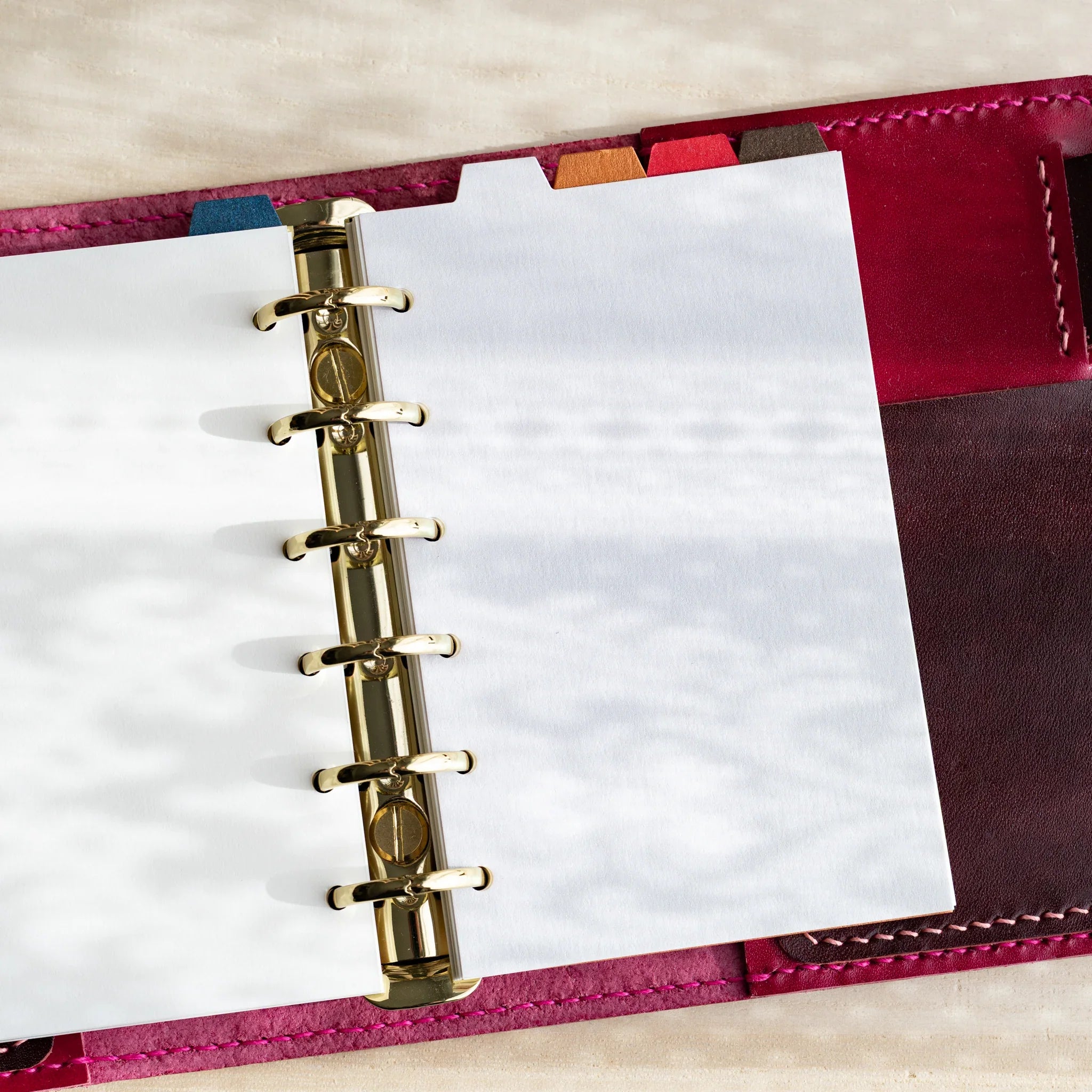 Japanese Stationery pale blue onion skin refill sheets in a mini 6 planner with gold rings and red leather cover on a desk.