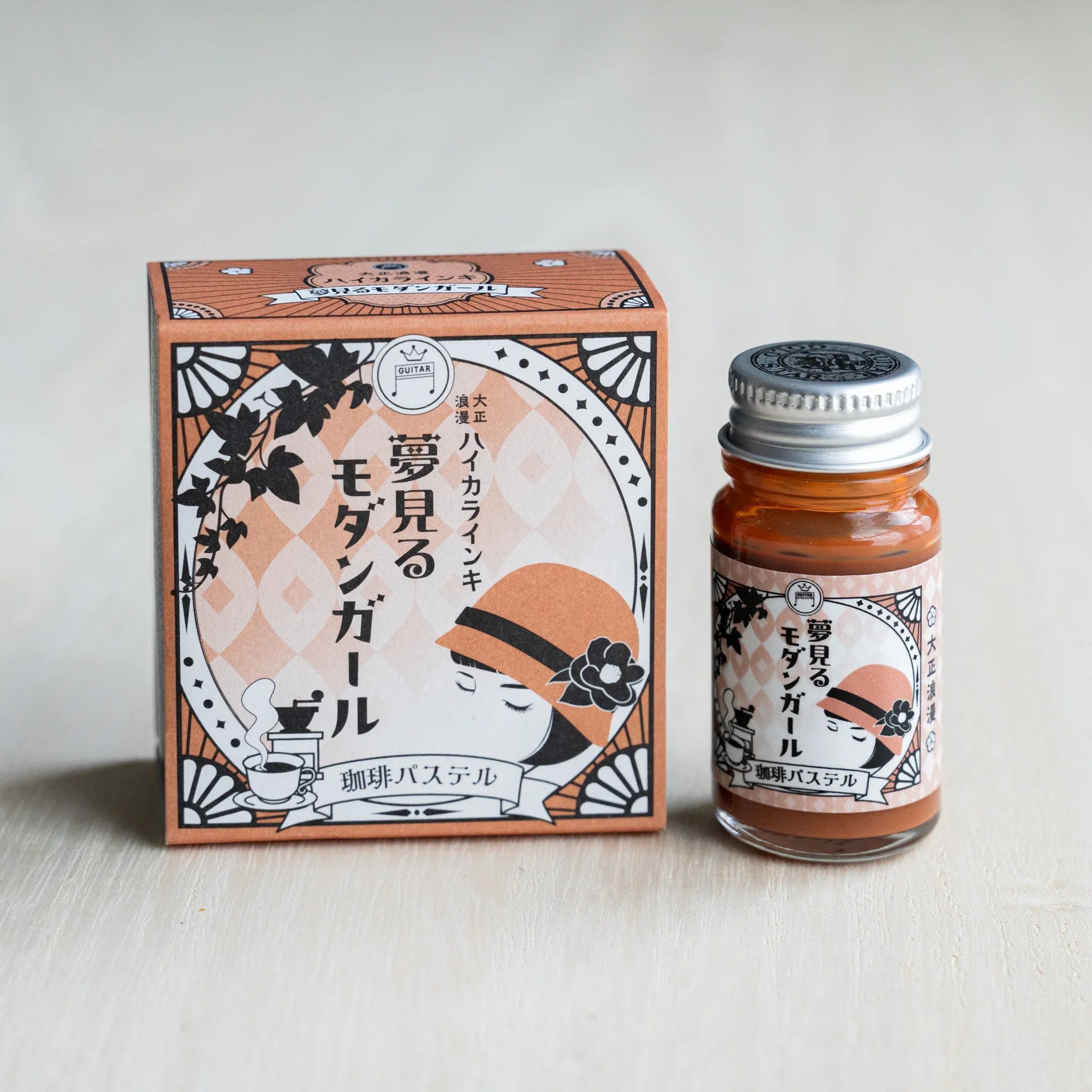Taisho Romance Coffee Pastel ink box in tan beside a 12 ml glass bottle of opaque reddish brown pigment ink