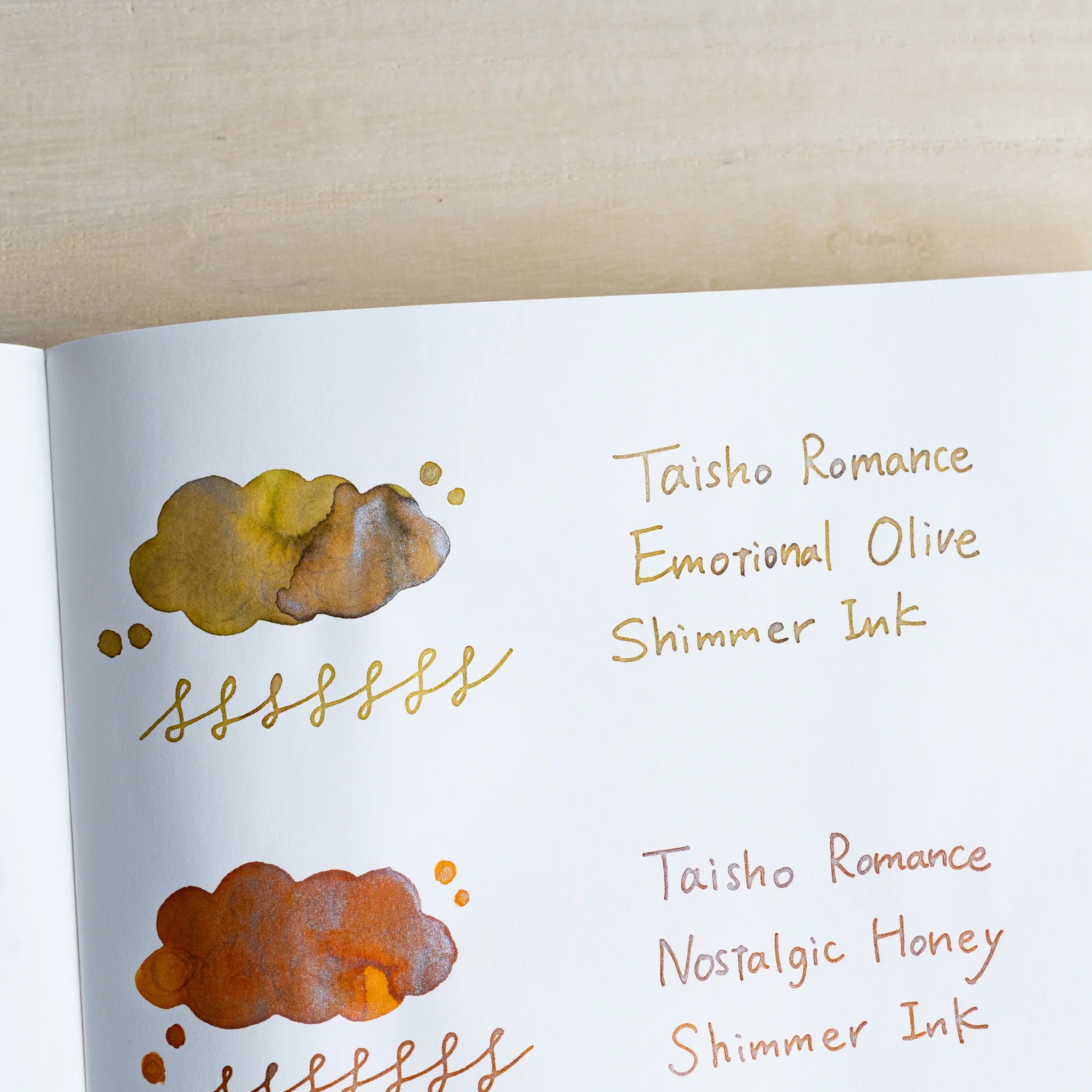 Handwritten swatch of Taisho Romance Emotional Olive Shimmer Ink, a cloud-shaped wash and looped line with silver flecks