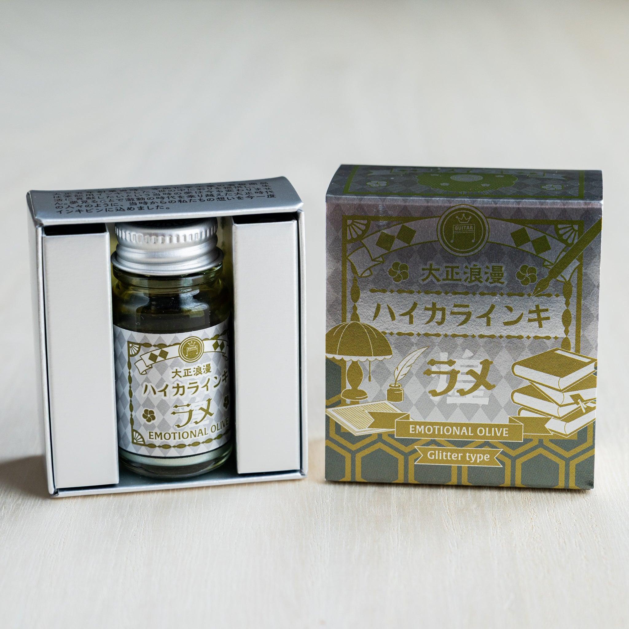 Taisho Romance Emotional Olive Shimmer Ink bottle in its open black inner box beside the closed silver foil outer box