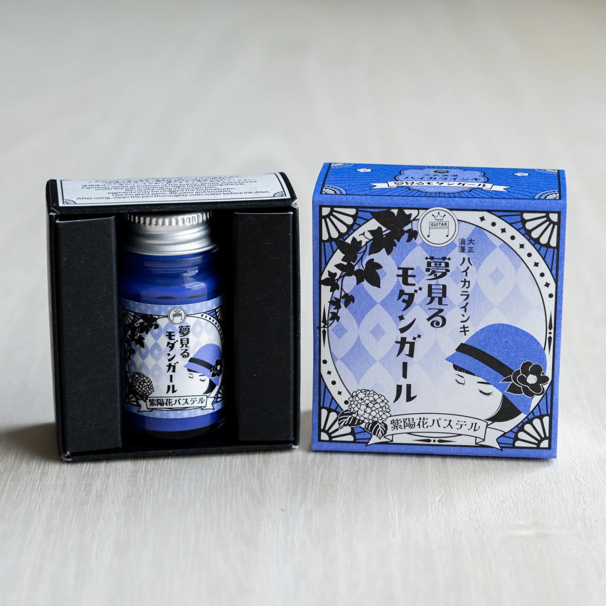 Taisho Romance Hydrangea Pastel ink bottle in its open black inner box, next to the closed periwinkle blue outer box