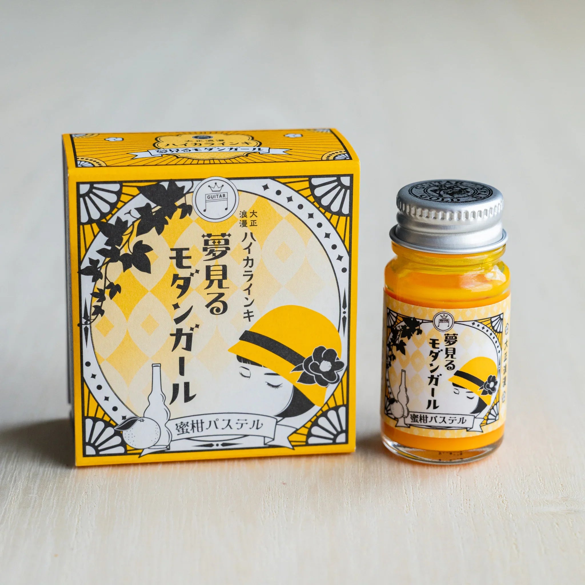 Taisho Romance Mandarin Pastel ink box in golden yellow beside a 12 ml glass bottle of opaque orange pigment ink