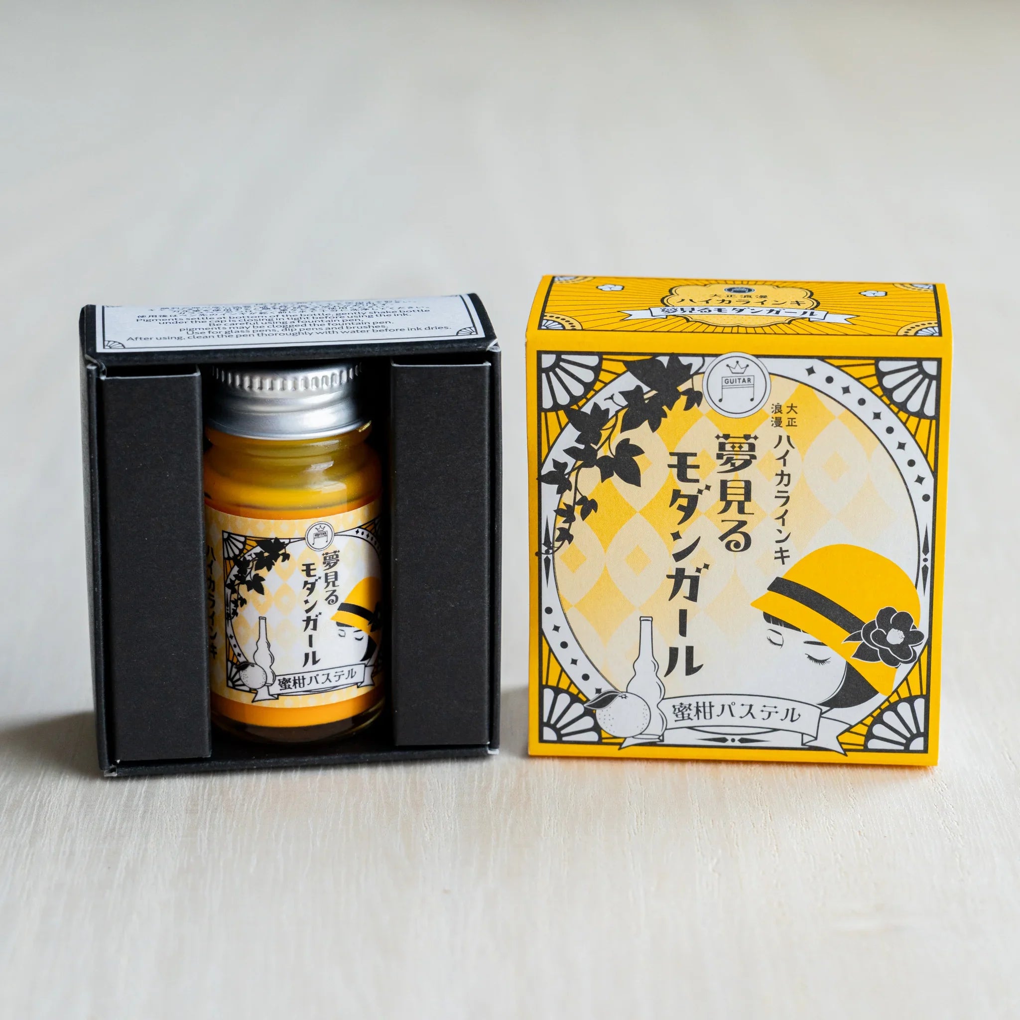 Taisho Romance Mandarin Pastel ink bottle in its open black inner box, next to the closed golden yellow outer box