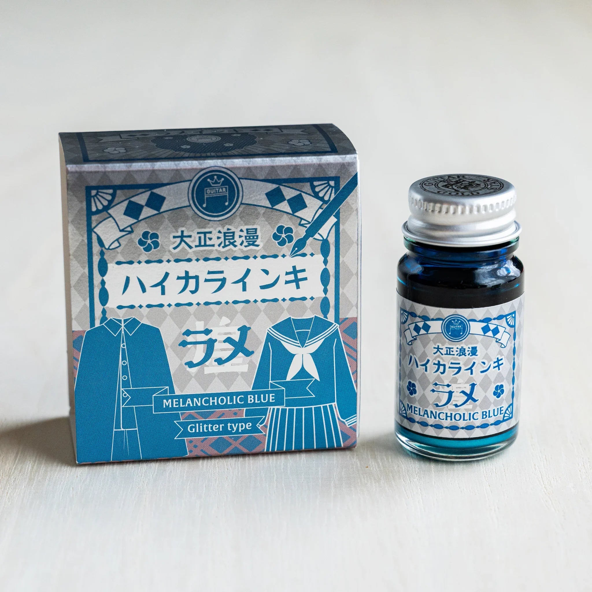 Taisho Romance Melancholic Blue Shimmer Ink silver foil box beside a 12 ml glass bottle of teal blue glitter ink