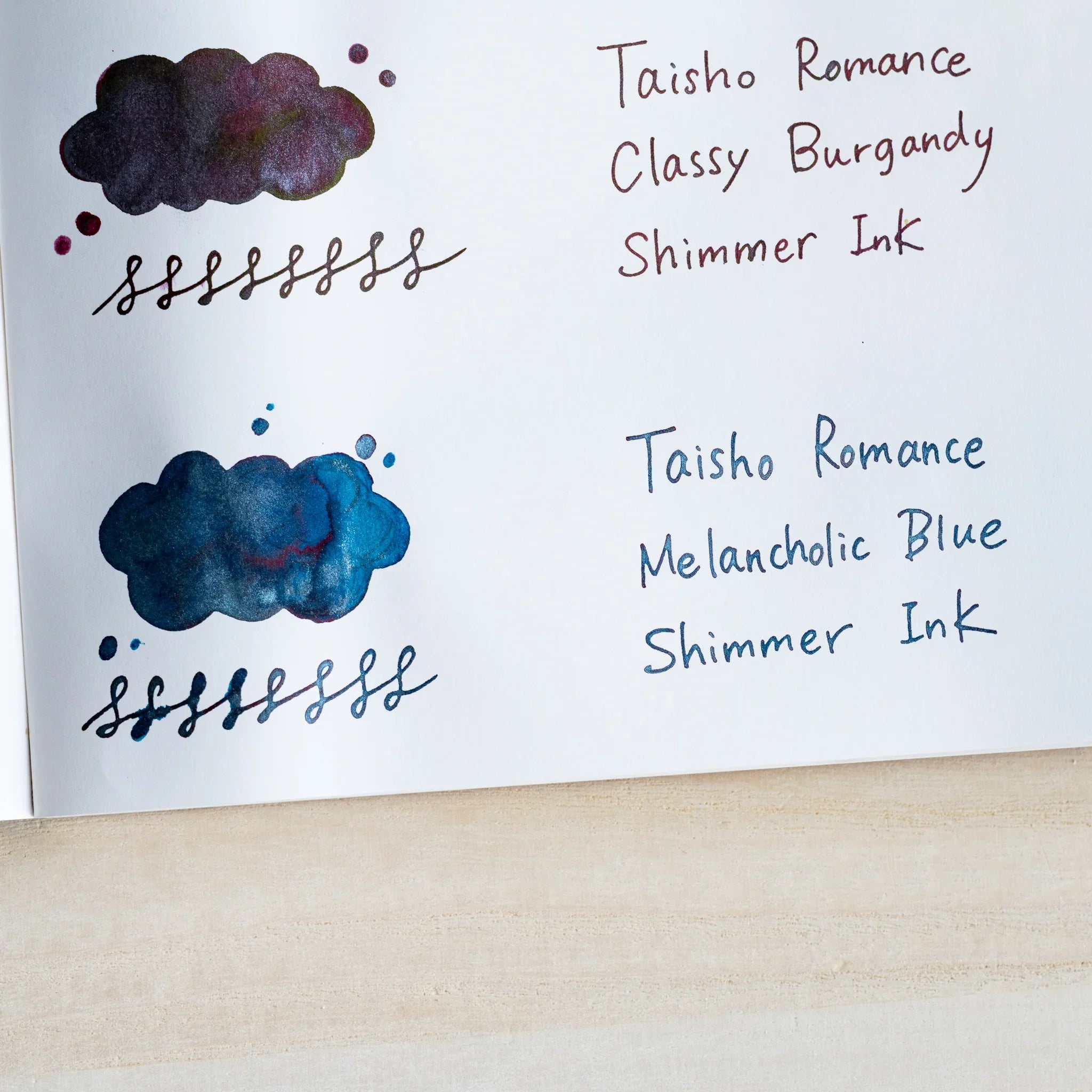 Handwritten swatch of Taisho Romance Melancholic Blue Shimmer Ink, a cloud-shaped wash and looped line with silver flecks