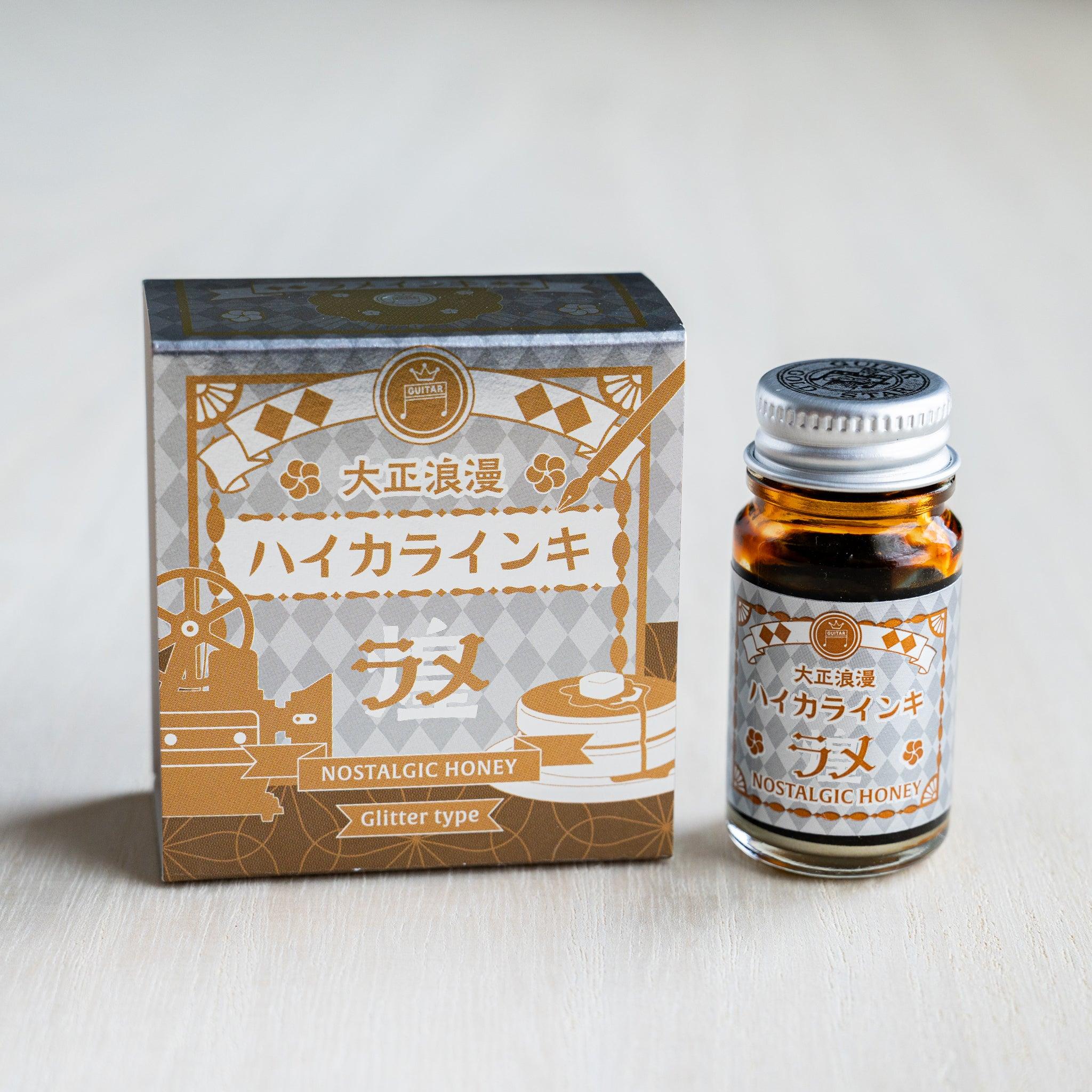 Taisho Romance Nostalgic Honey Shimmer Ink silver foil box beside a 12 ml glass bottle of amber glitter ink