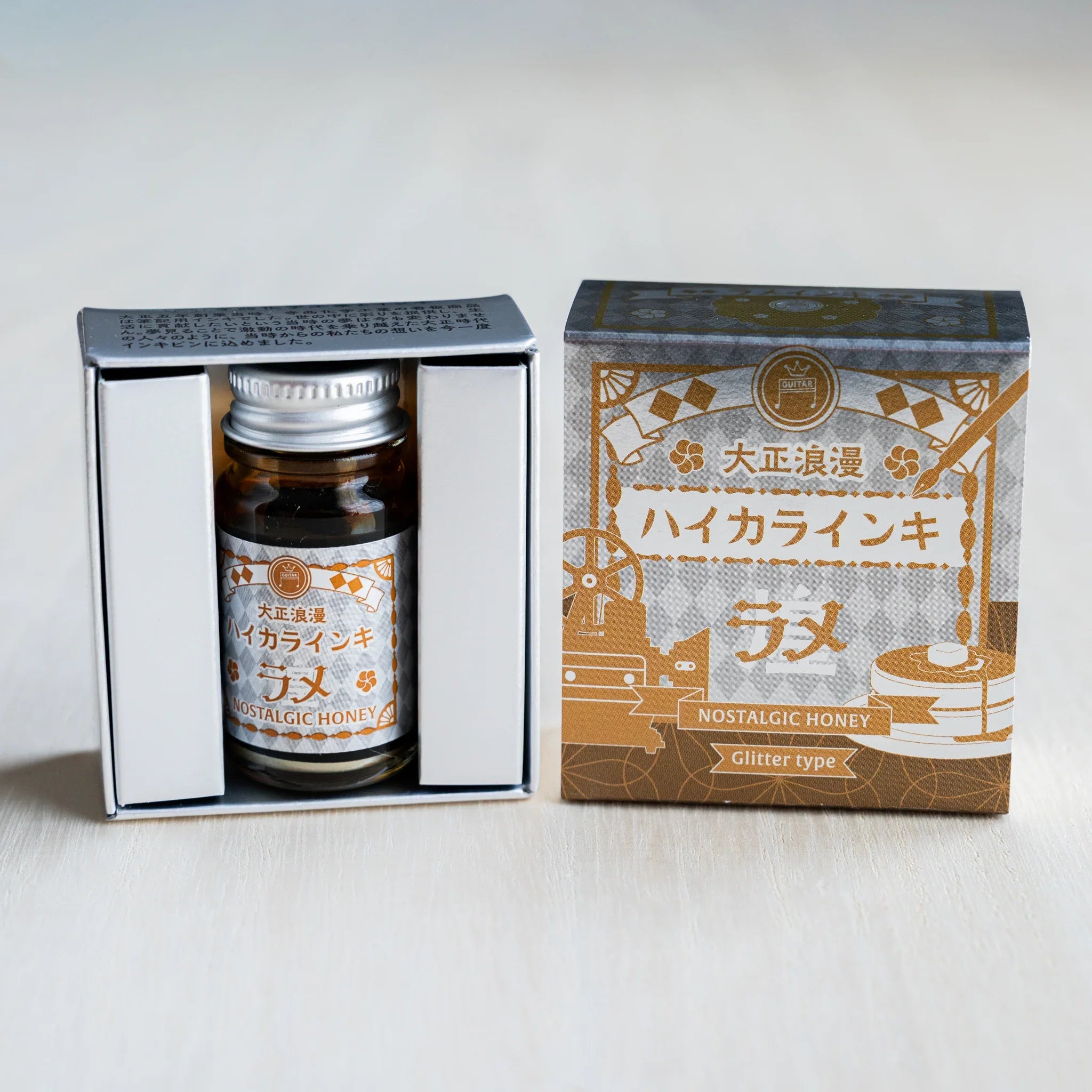 Taisho Romance Nostalgic Honey Shimmer Ink bottle in its open black inner box beside the closed silver foil outer box