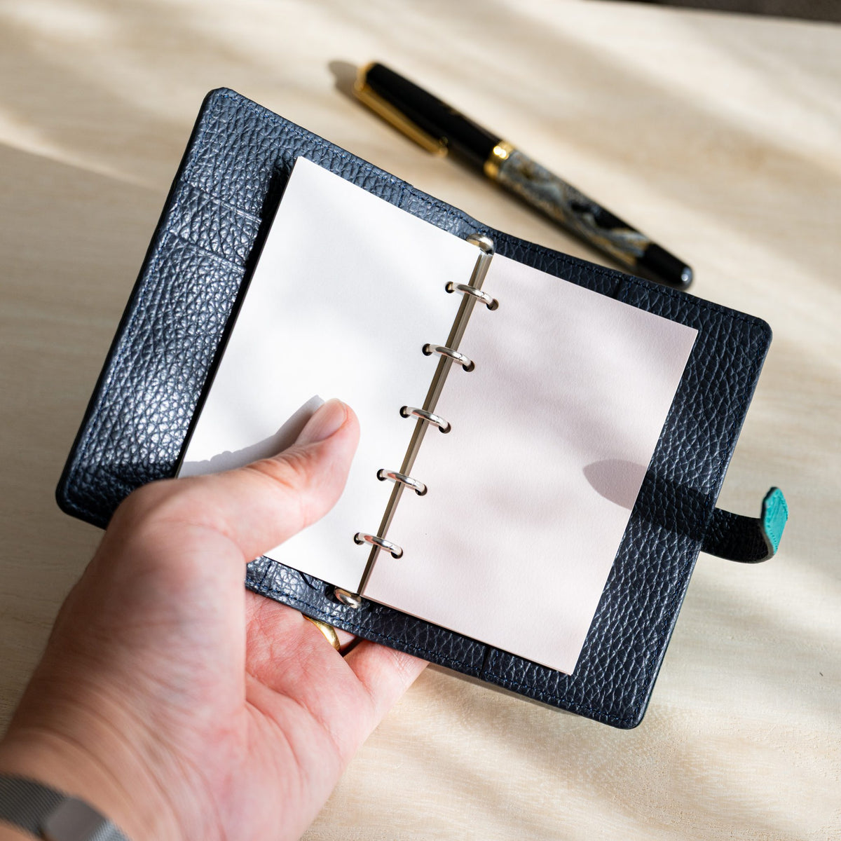 Hand holding an open navy planner showing white and primrose Araveal M5 refill pages
