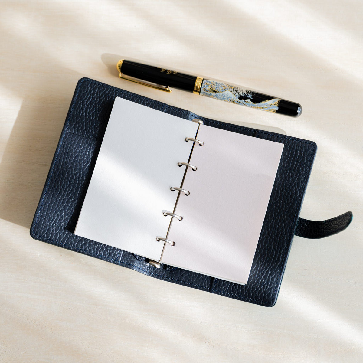 Open navy planner with white and primrose Araveal M5 refill pages, black and gold fountain pen above