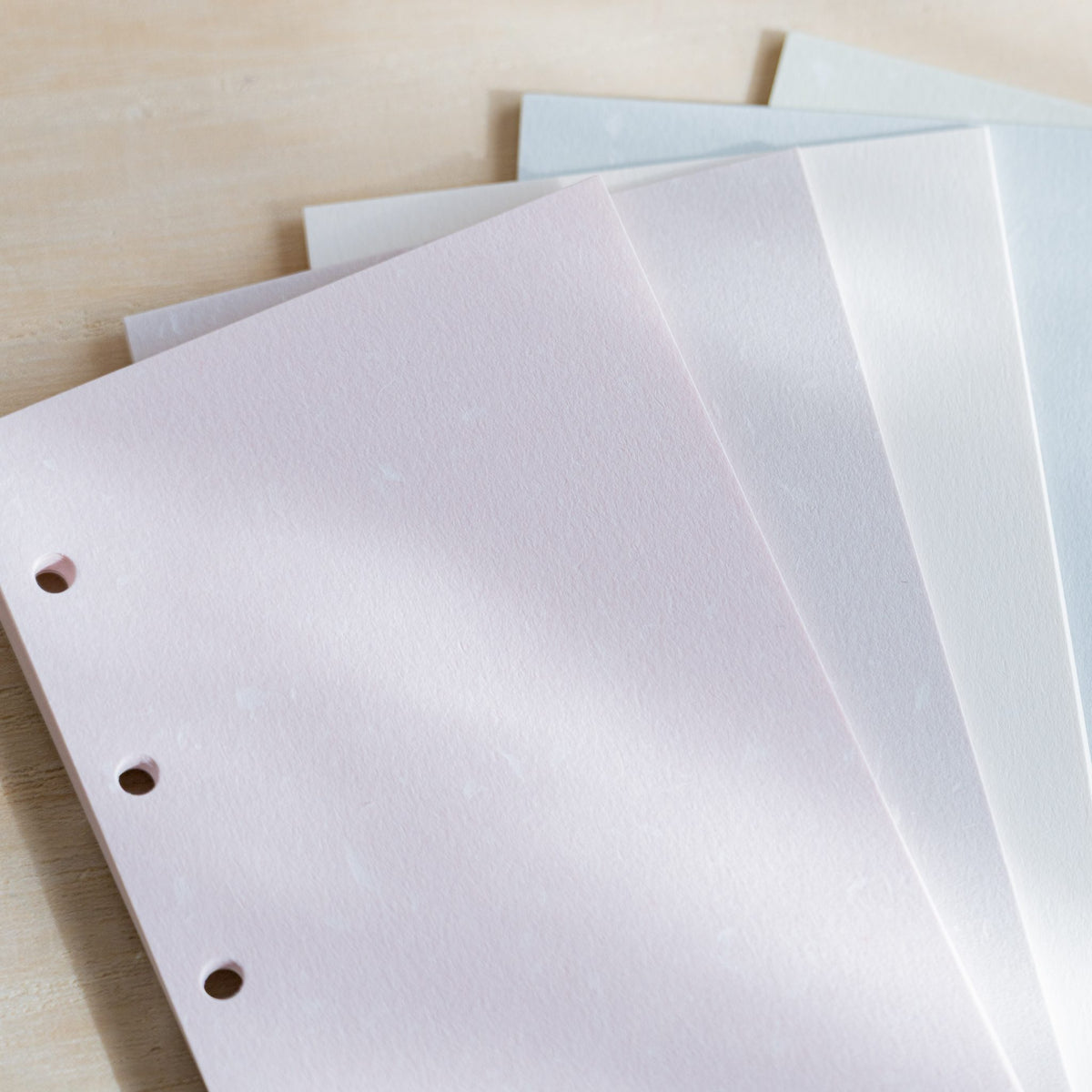 Close-up of Feather Waltz M5 refill sheets in pale pink, white and light blue with punched holes