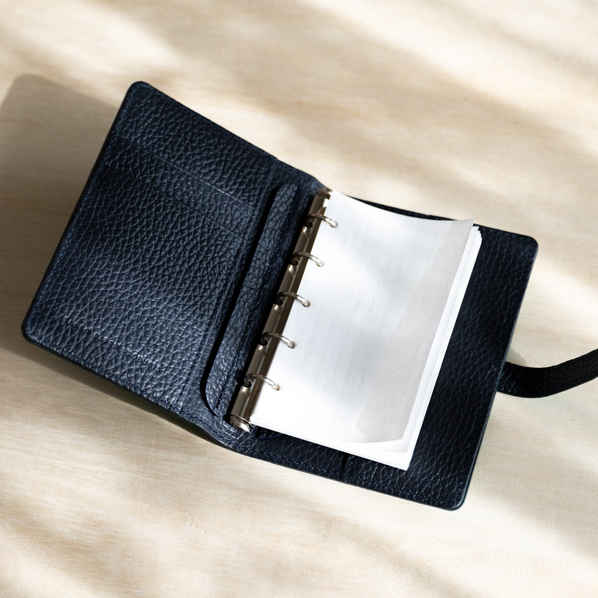 White KateJo Onion Skin M5 refill curling on the rings of an open Ise Gikakushi M5 planner with navy leather interior