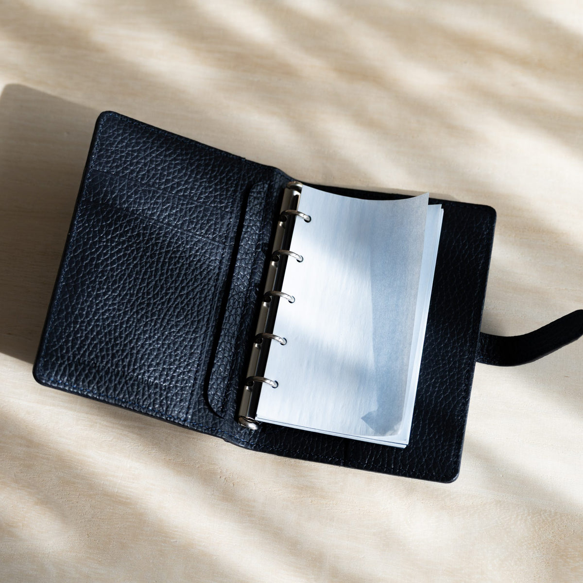 Pale blue KateJo Onion Skin M5 refill on the silver rings of an open navy grained leather planner