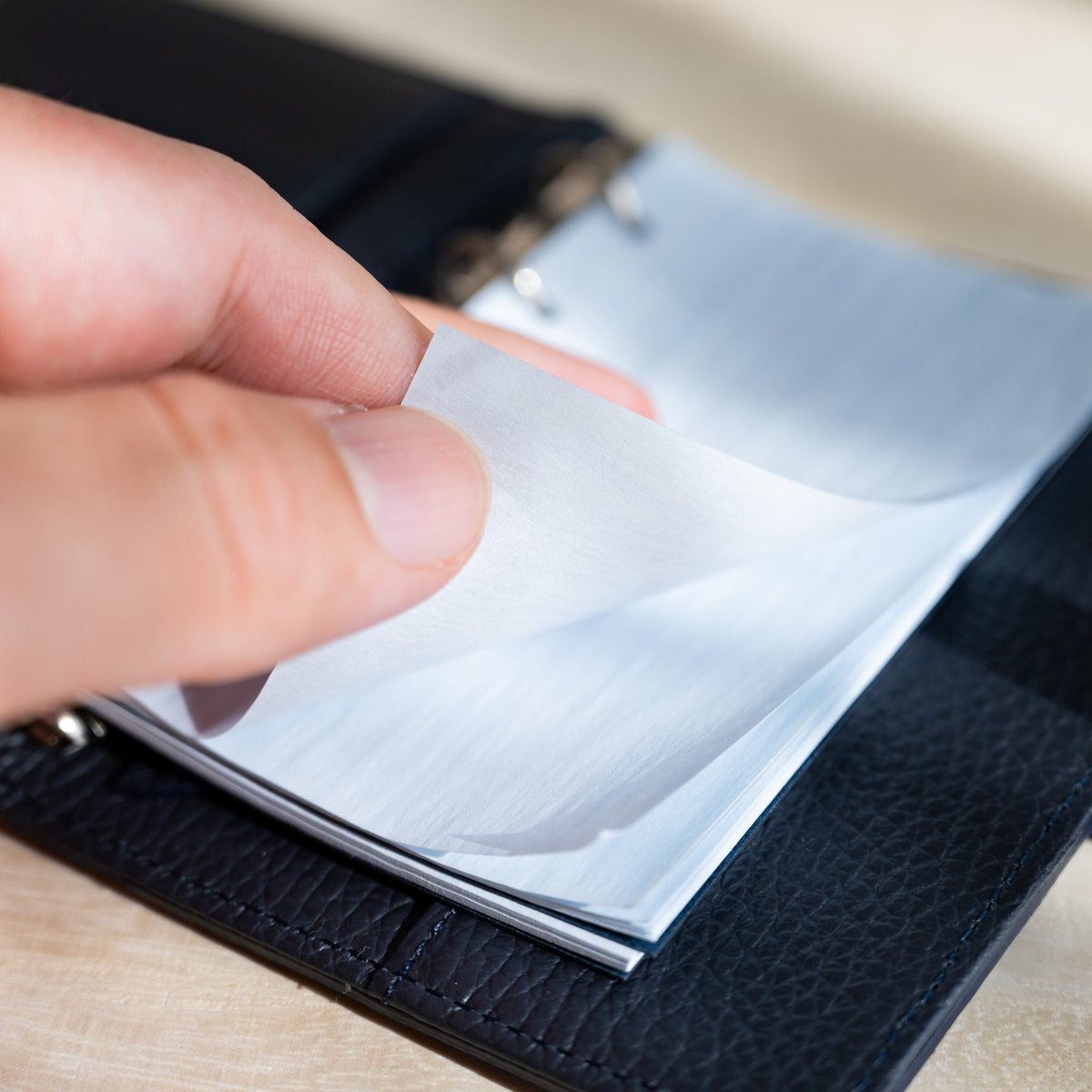 Fingers lifting a thin pale blue KateJo Onion Skin sheet with crinkled texture in a navy planner