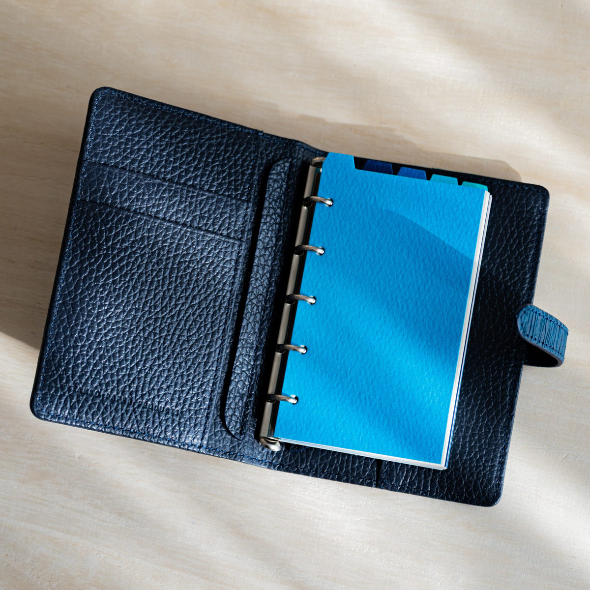 Sky blue Mermaid M5 divider on the silver rings of an open navy grained leather planner