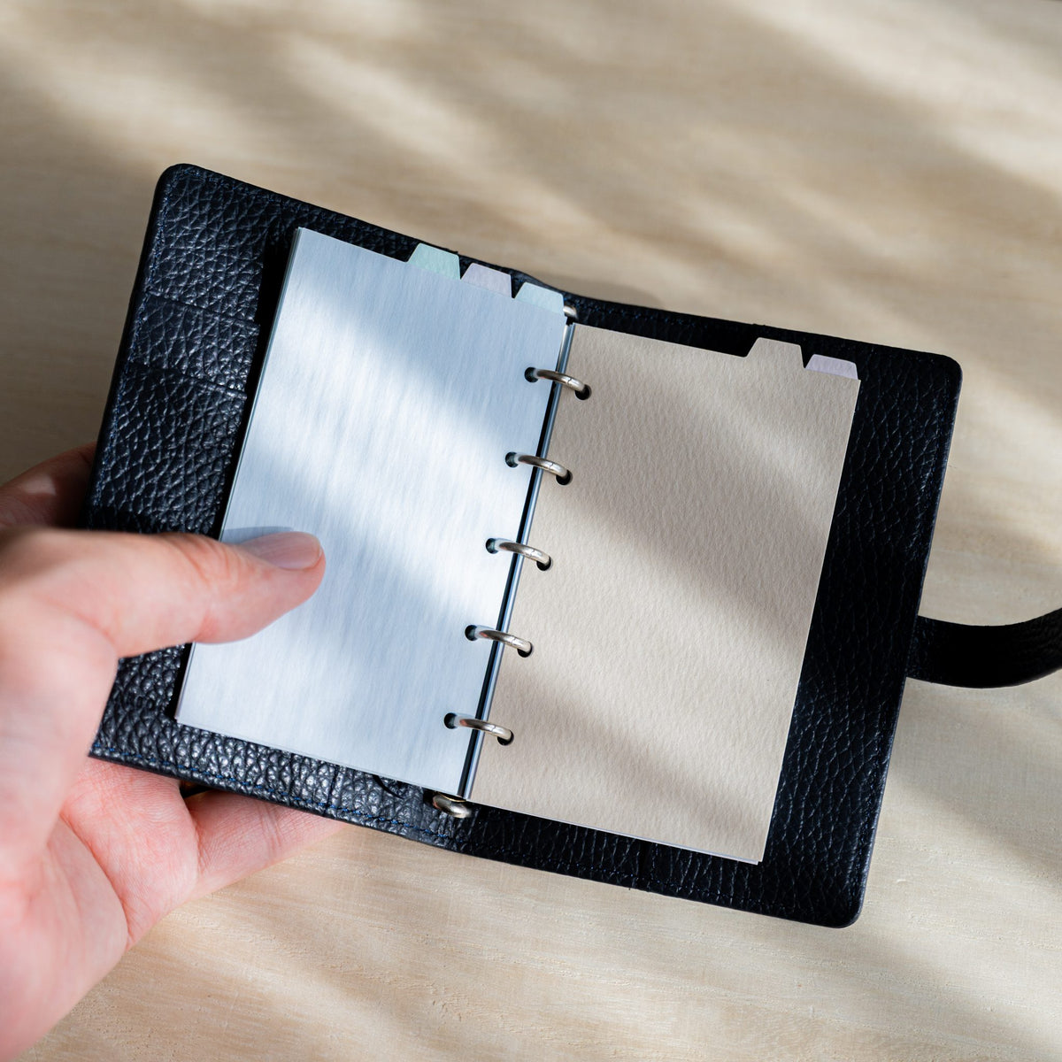 Hand holding an open navy planner with a Mermaid M5 divider and an ecru divider on the right