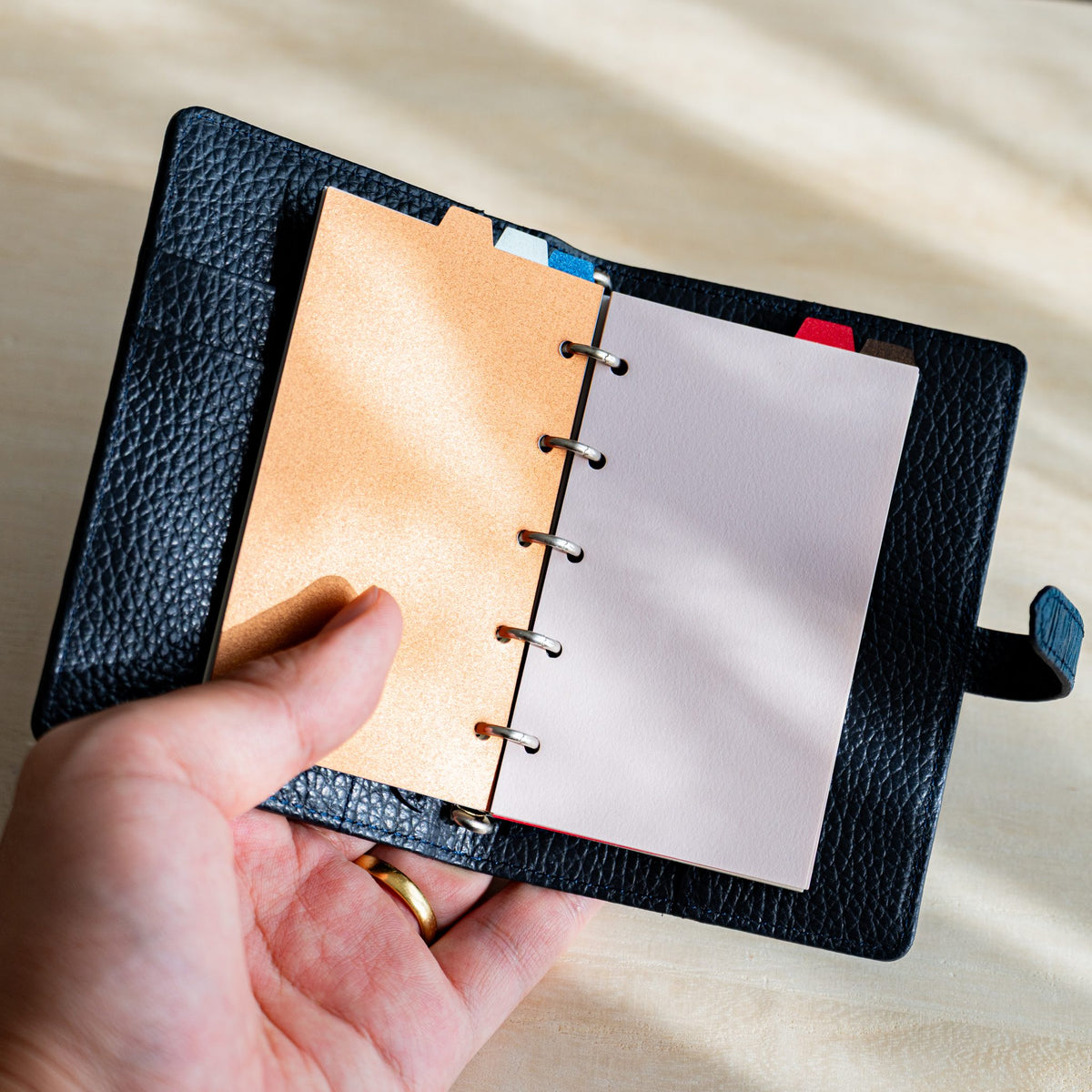 Hand holding an open navy planner showing a copper Stardream divider beside a pale pink page