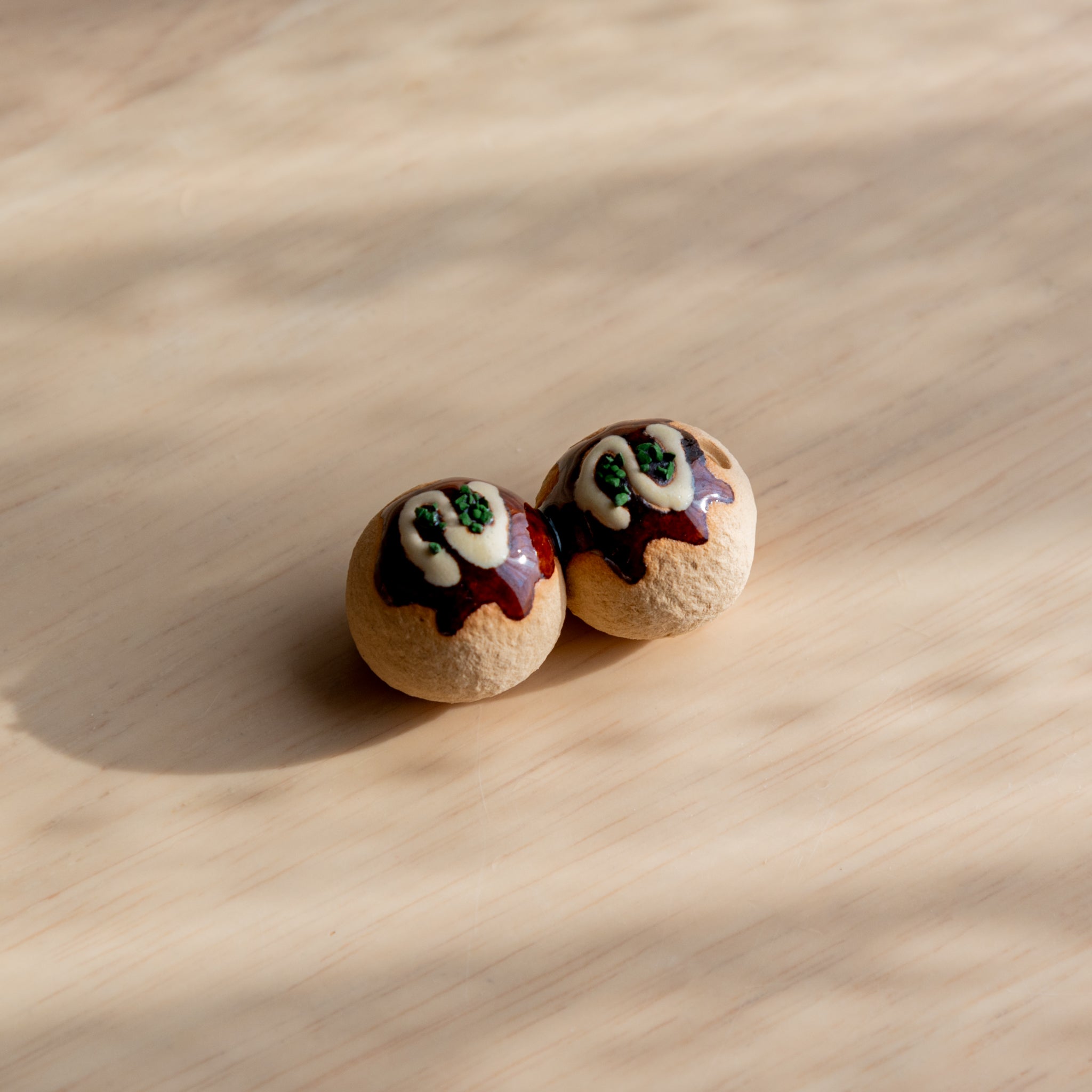 Two takoyaki-shaped Japanese pen rests with detailed toppings on a light wooden surface.