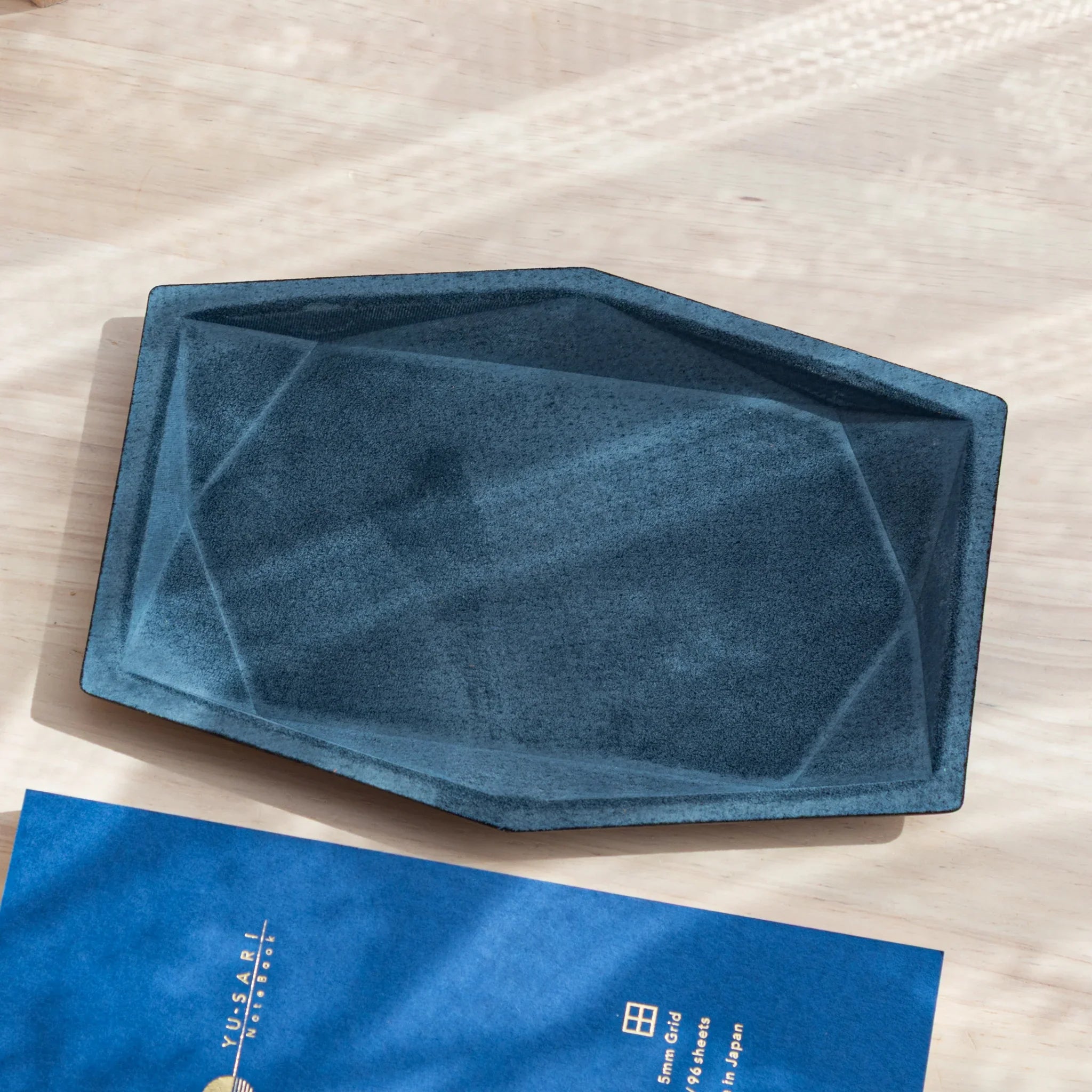 Japanese Pen Tray with angular blue suede design placed on desk.