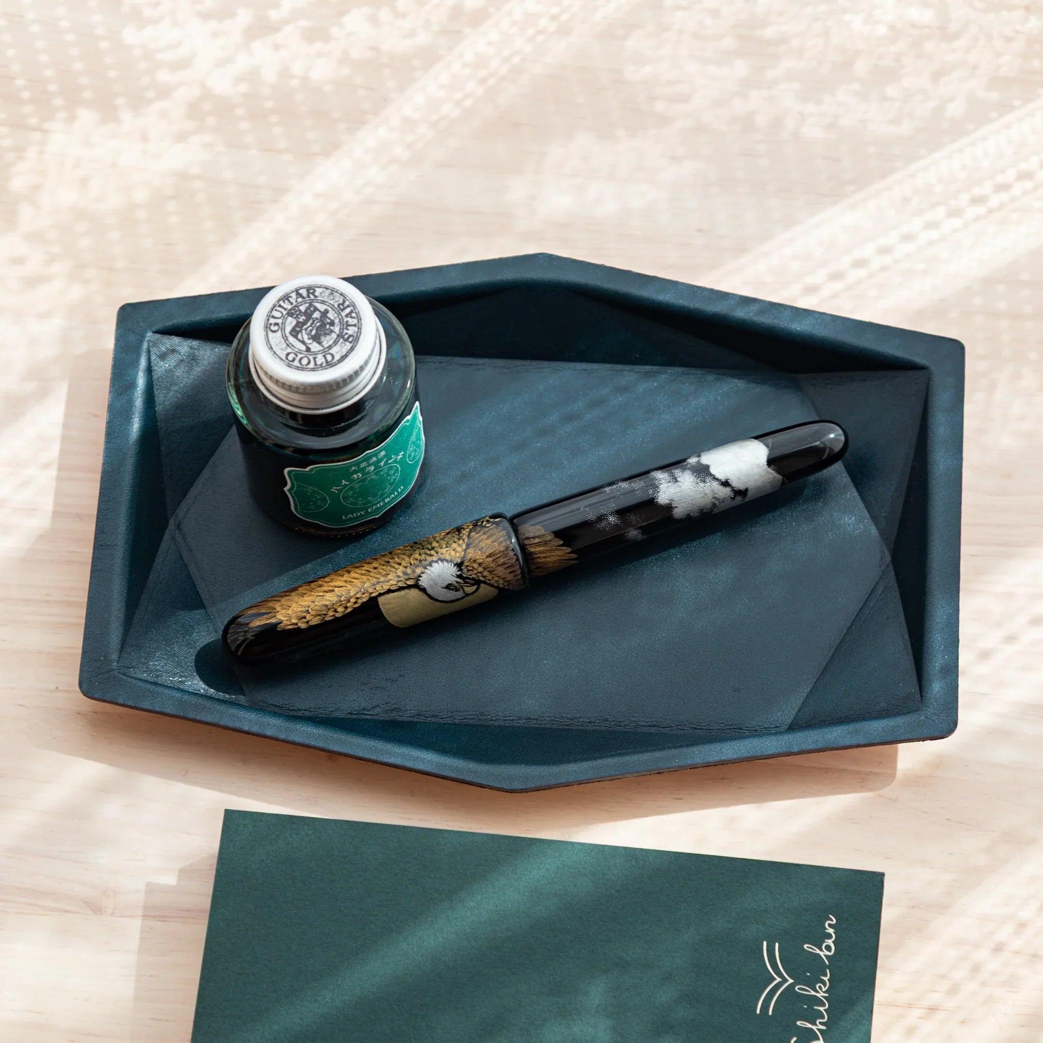Japanese Pen Tray in Teal-Blue leather holding a Japanese Fountain Pen and green ink bottle on a desk.