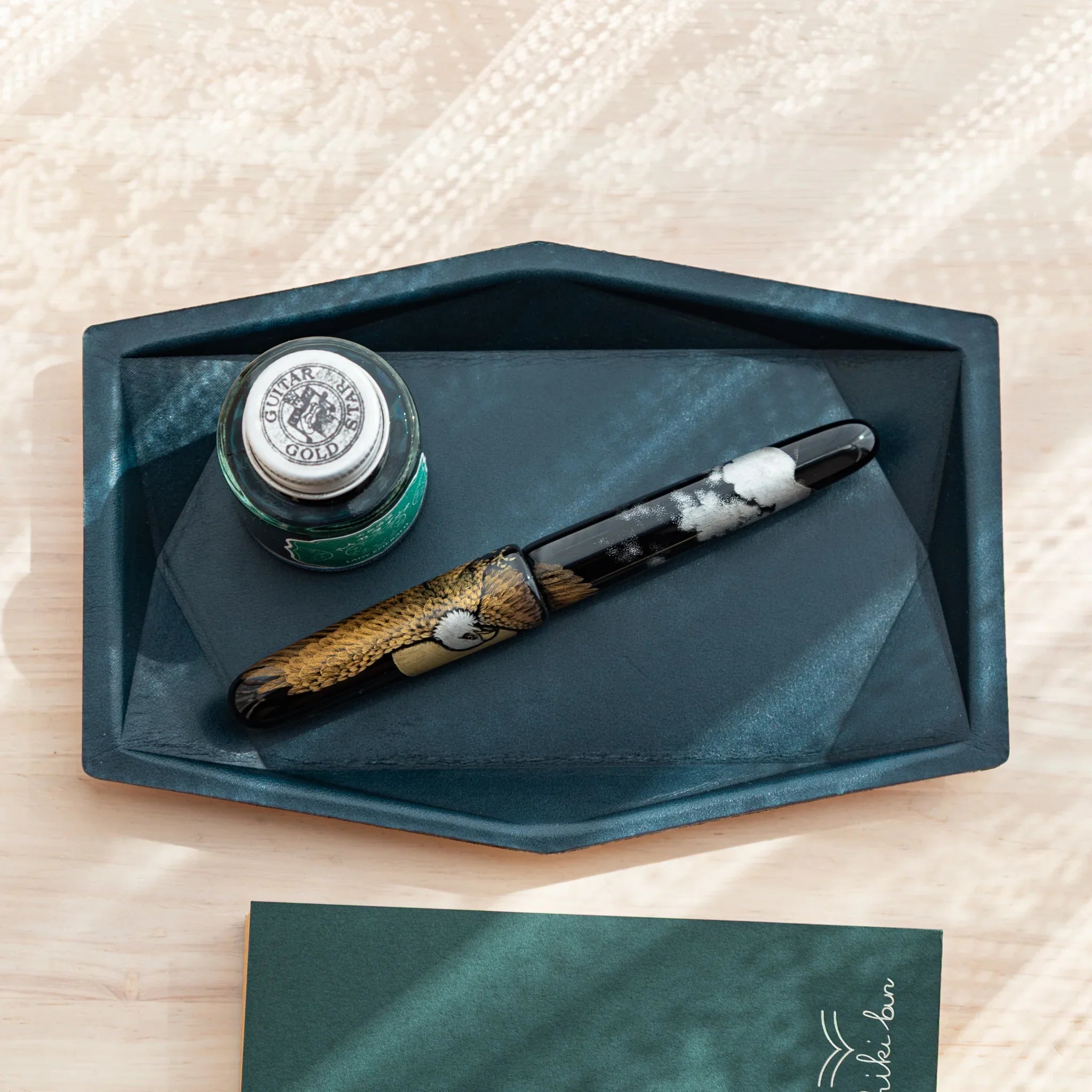 Japanese Pen Tray in Teal-Blue leather holding a Japanese Fountain Pen and green ink bottle on a desk.