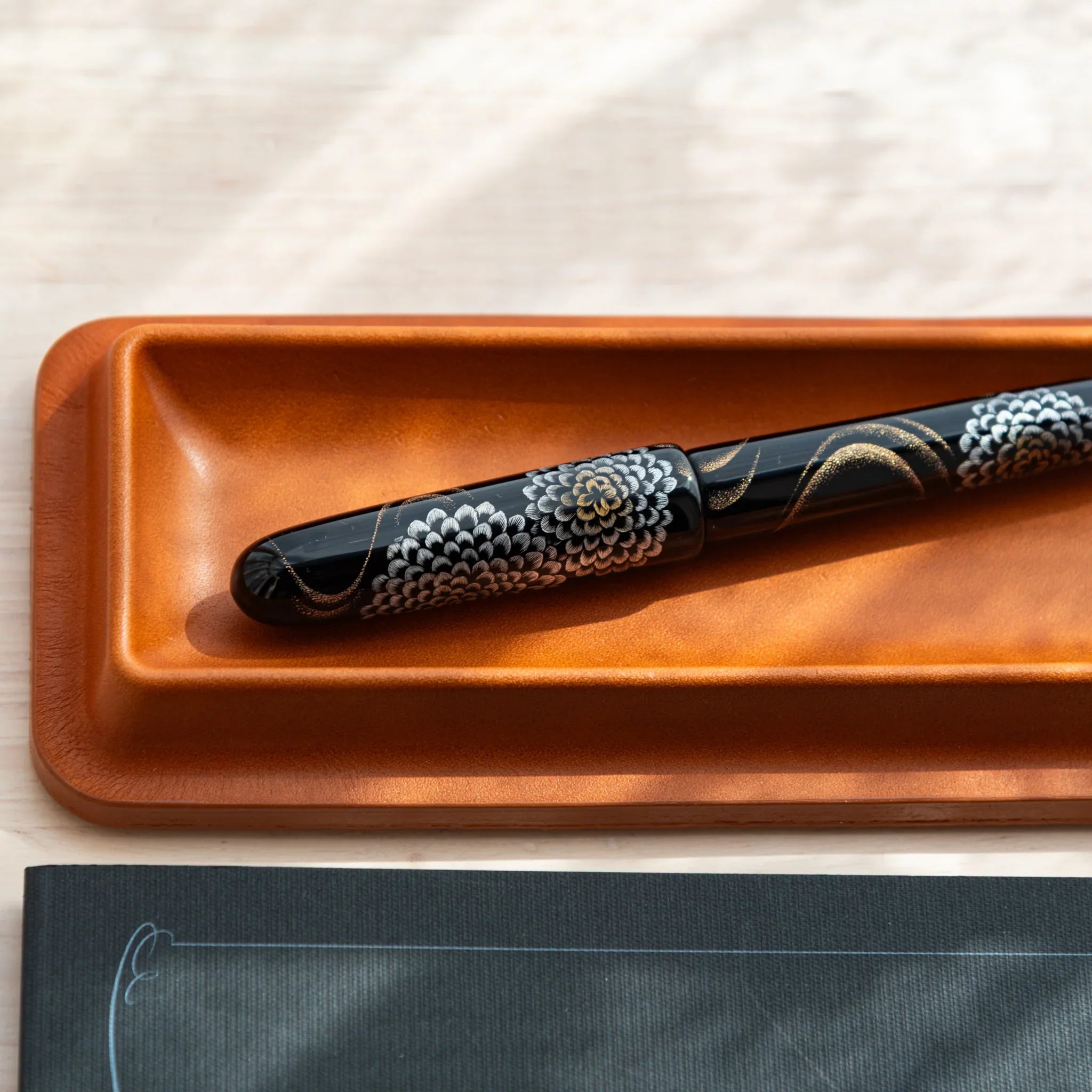 Japanese fountain pen with gold and silver floral maki-e placed in a Tatsuno leather pen tray.