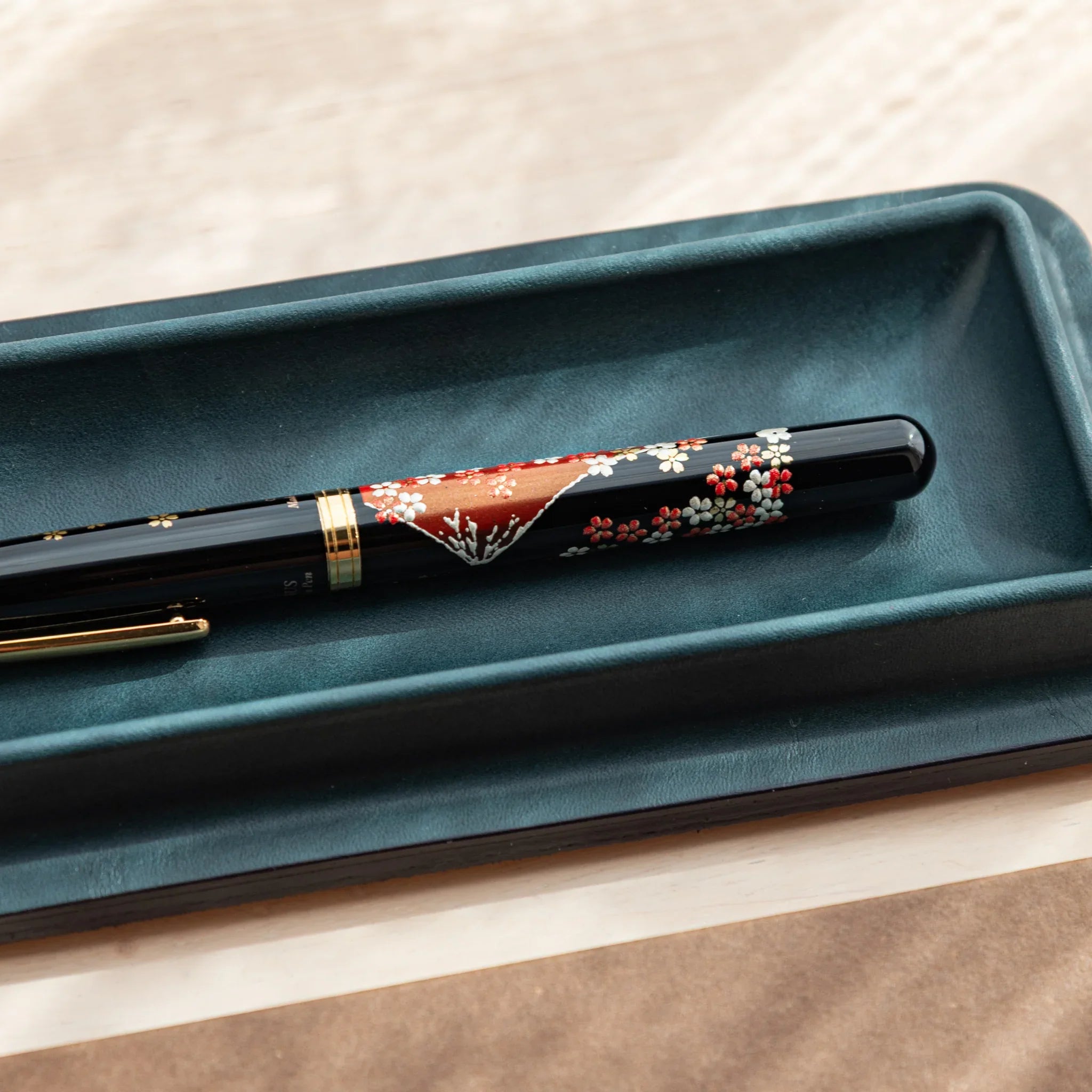 Close-up of floral Japanese Fountain Pen resting in the dark green Tatsuno Leather Pen Tray Slim.
