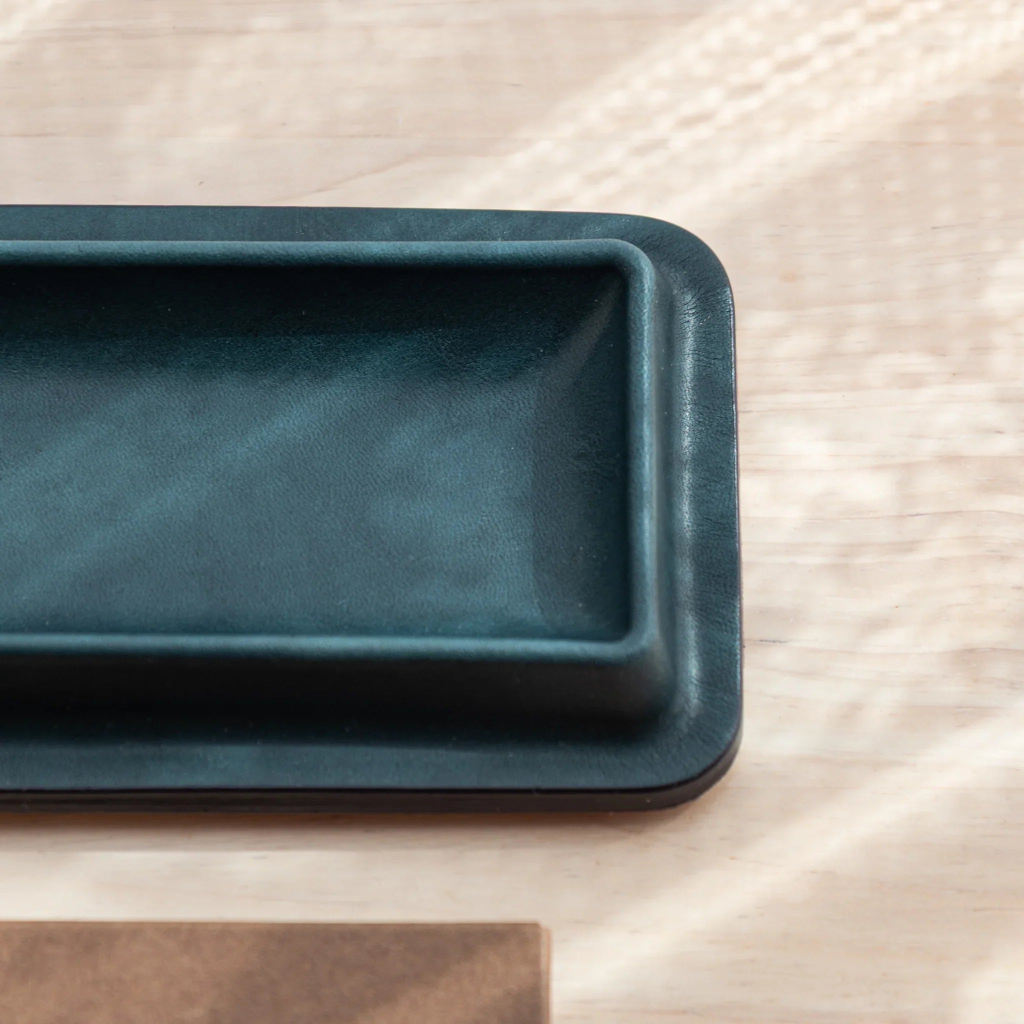 Corner close-up of empty green Tatsuno Leather Pen Tray Slim on light wood desk.