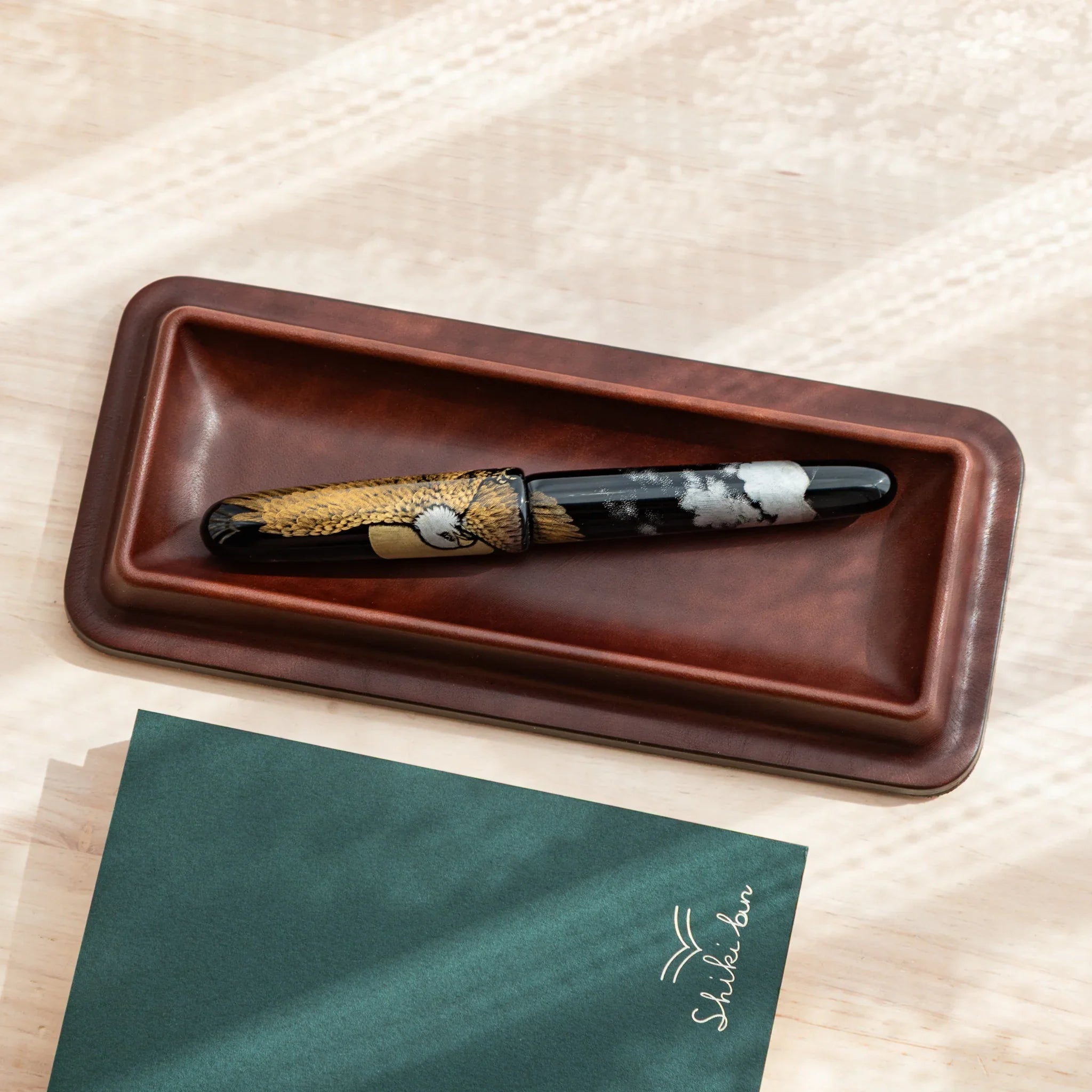 Japanese fountain pen with eagle motif placed in a dark brown Tatsuno leather pen tray.