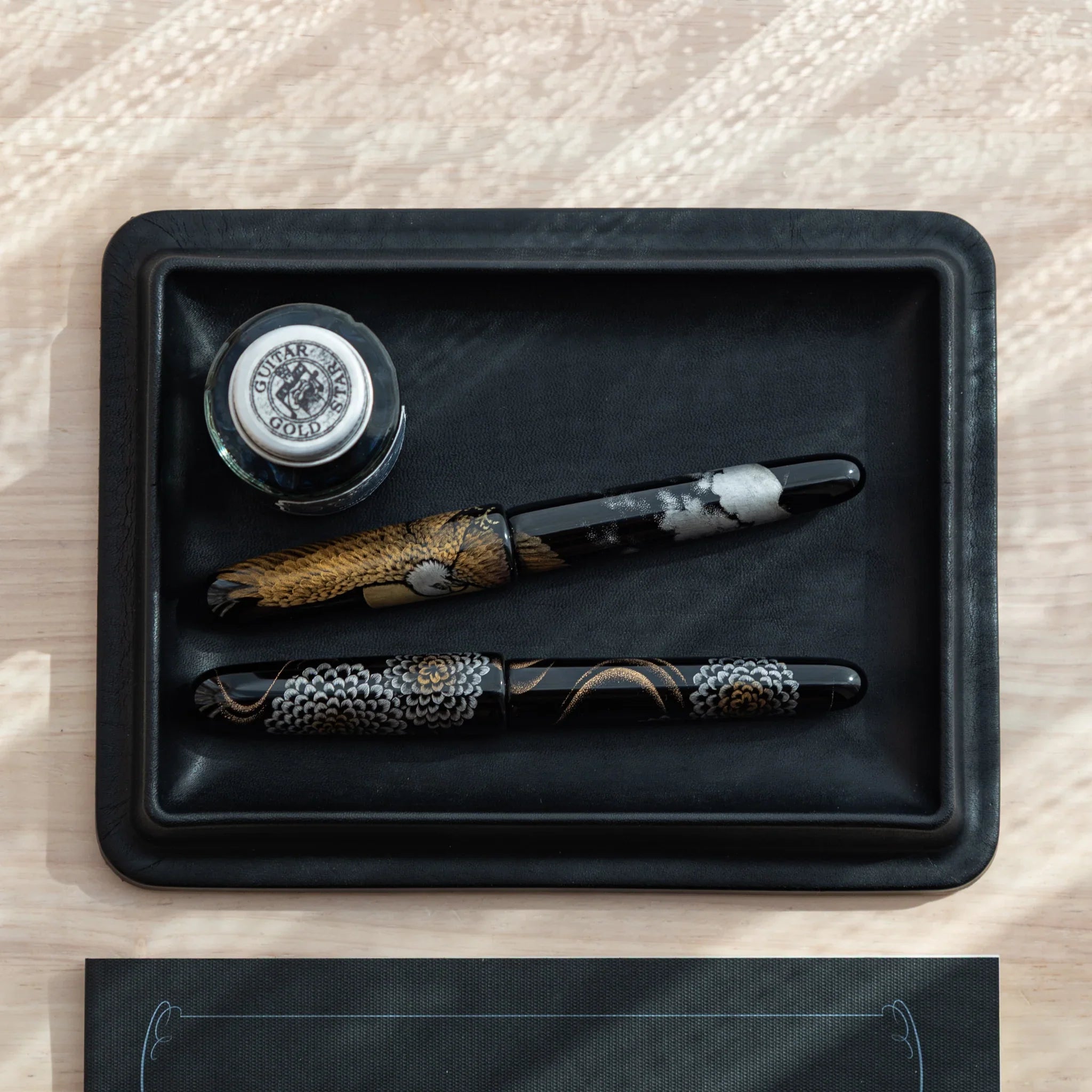 Japanese Pen Tray in black leather, shown with ink bottle and two Japanese fountain pens.