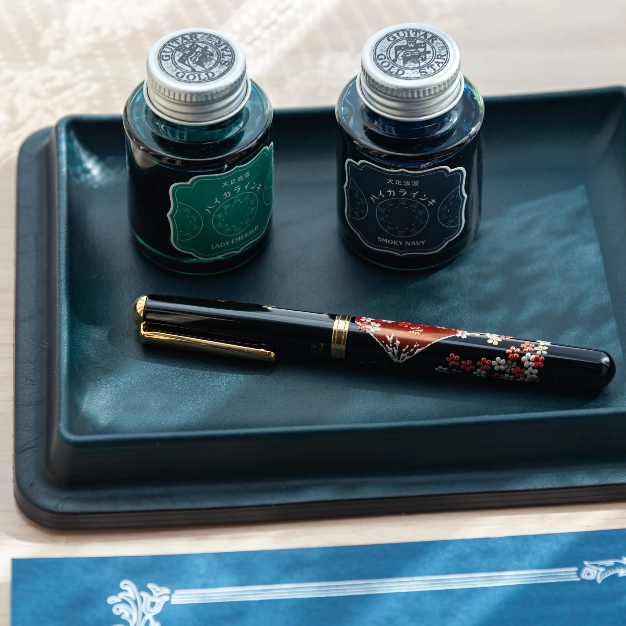 Japanese Pen Tray in deep blue leather, holding two ink bottles and a lacquered fountain pen.