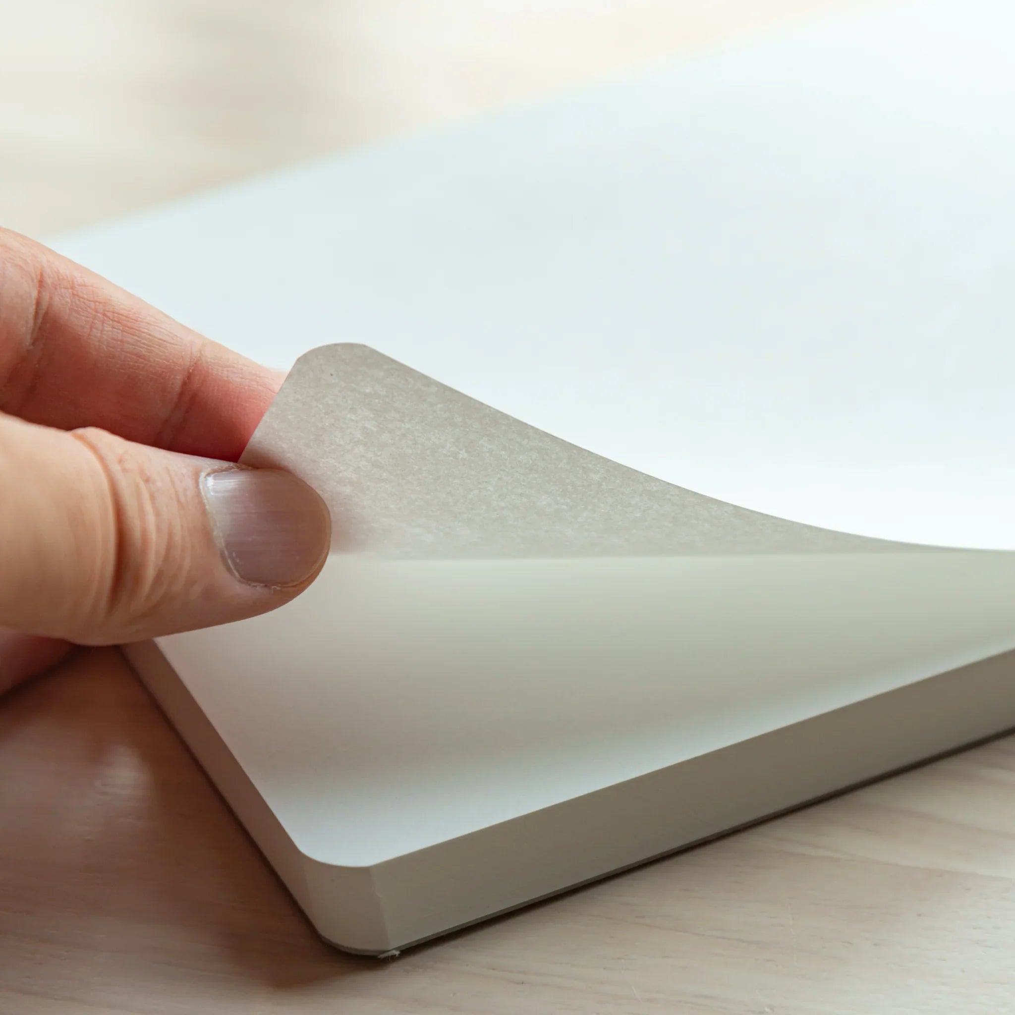 Close-up of the Tomoegawa Tomoe River A5 Writing Pad, showing smooth white paper with rounded corner on a wooden desk.