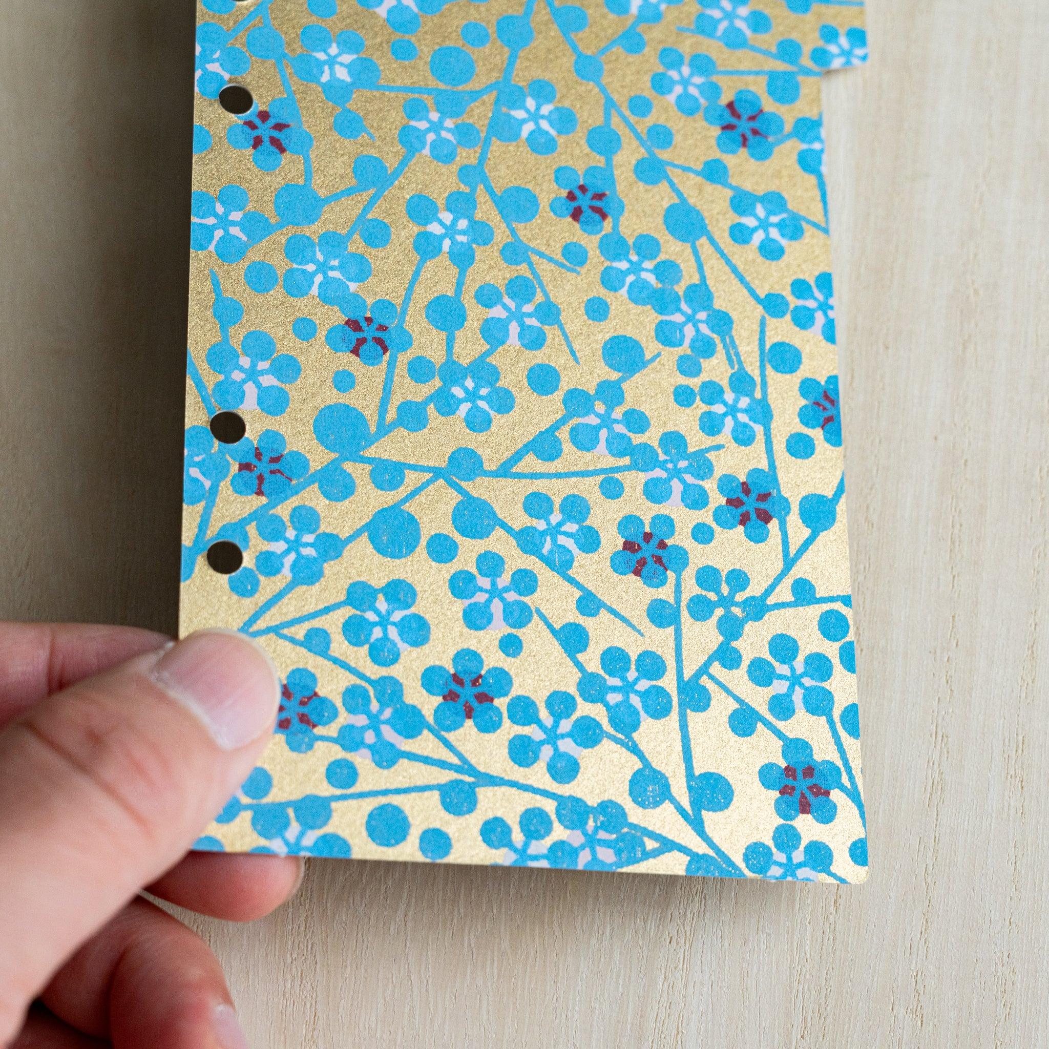 Hand holding a Tone index divider, close-up of turquoise plum blossoms on metallic gold hand-dyed washi