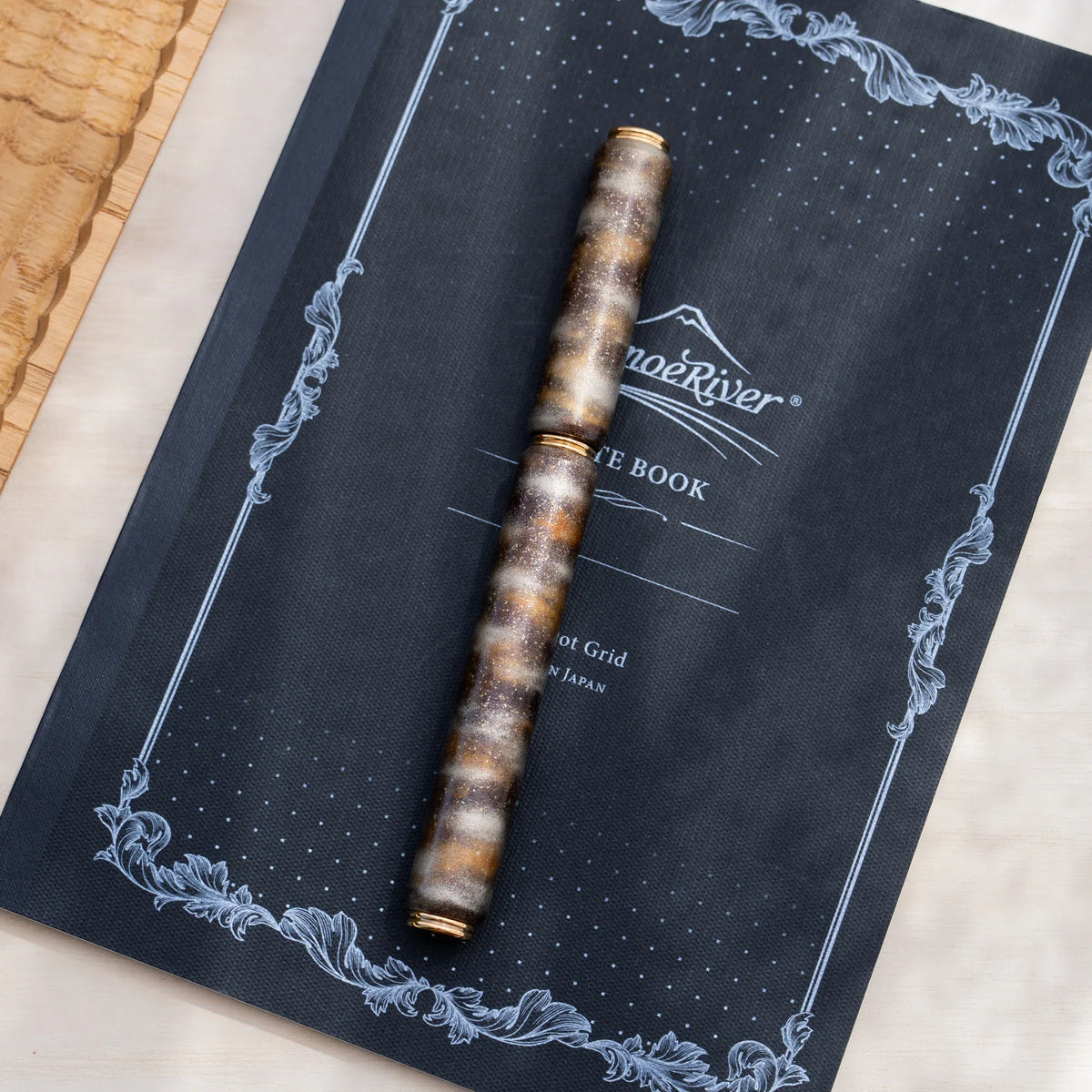 Translucent brown marbled urushi lacquered rollerball pen in zelkova wood, resting on a Japanese notebook
