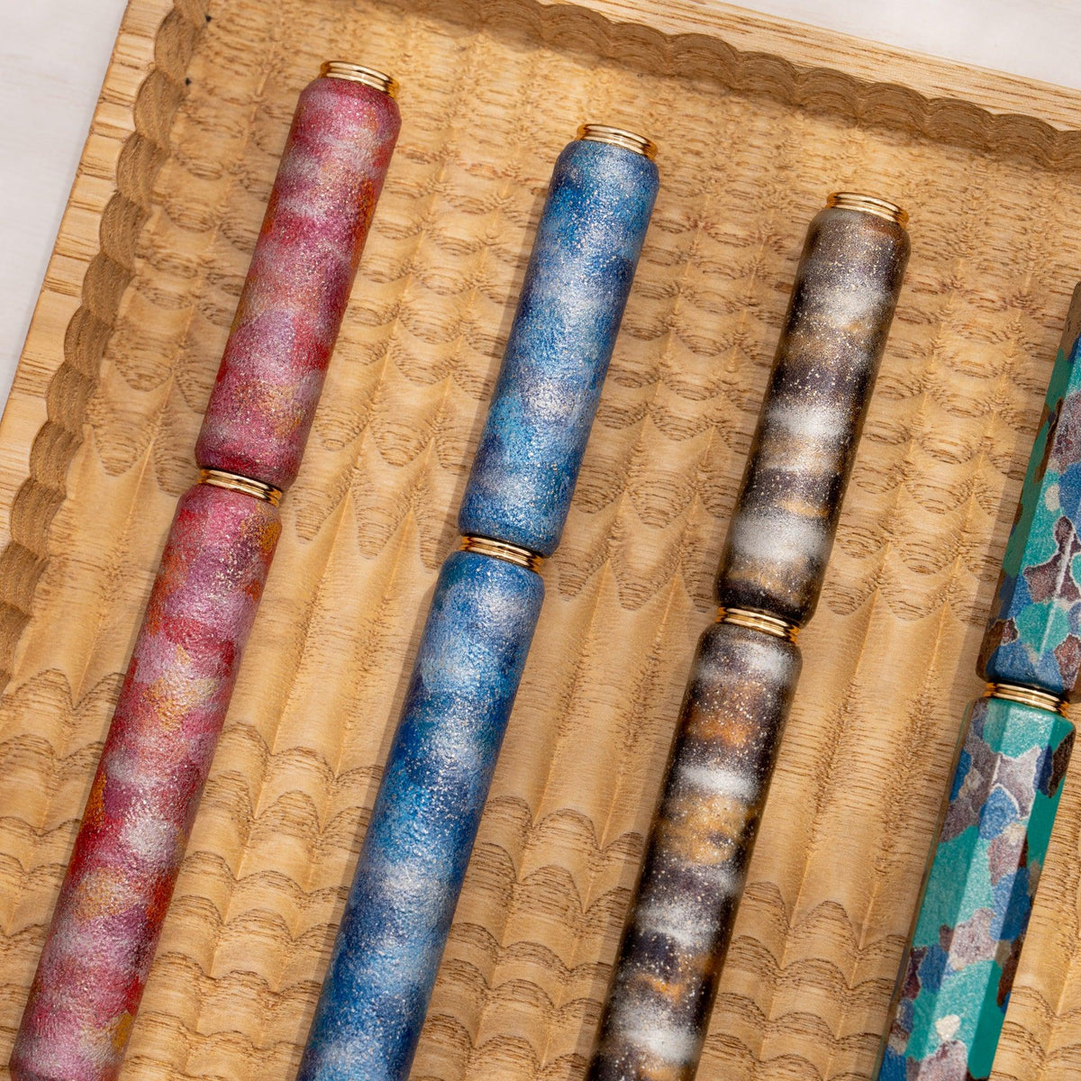 Five urushi lacquered rollerball pens by Toshiyuki Tatsumi and Toshiyuki Tatsumi in a wooden tray