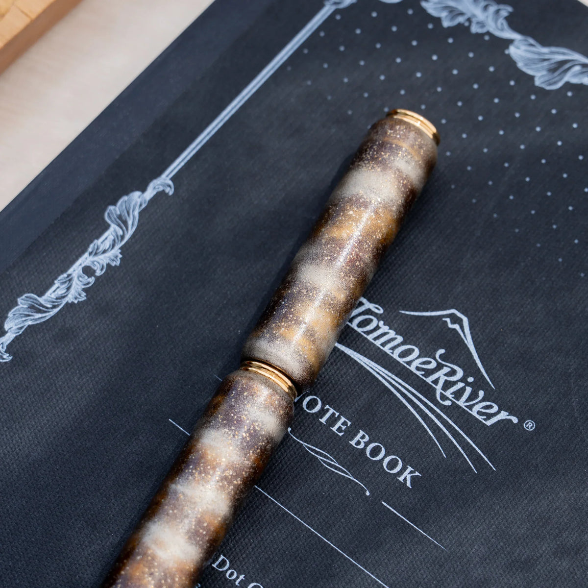 Translucent brown marbled urushi lacquered rollerball pen in zelkova wood, resting on a Japanese notebook
