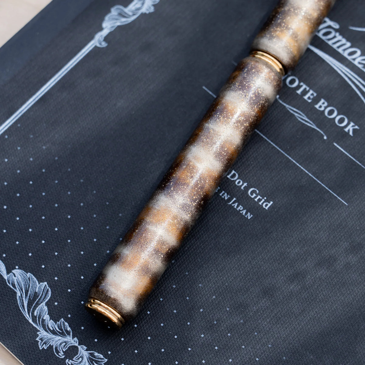 Translucent brown marbled urushi lacquered rollerball pen in zelkova wood, resting on a Japanese notebook