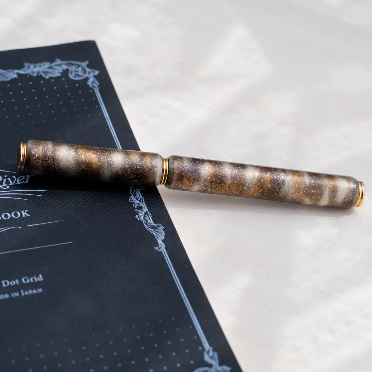 Translucent brown marbled urushi lacquered rollerball pen in zelkova wood with the cap removed, showing the barrel and gold trim