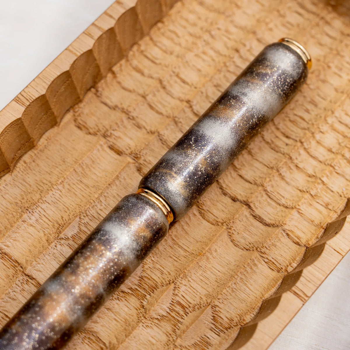 Close-up of the marbled color urushi surface on the translucent brown zelkova wood rollerball pen