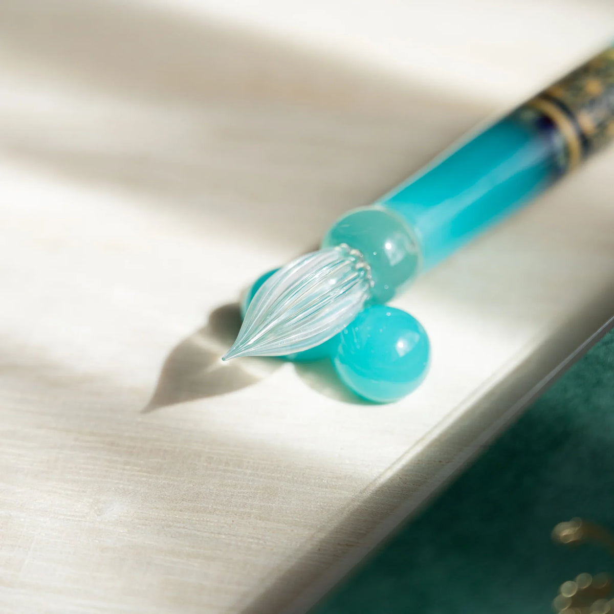 Clear ribbed nib of the Turquoise Hemp Leaves glass dip pen tilted onto a turquoise glass sphere